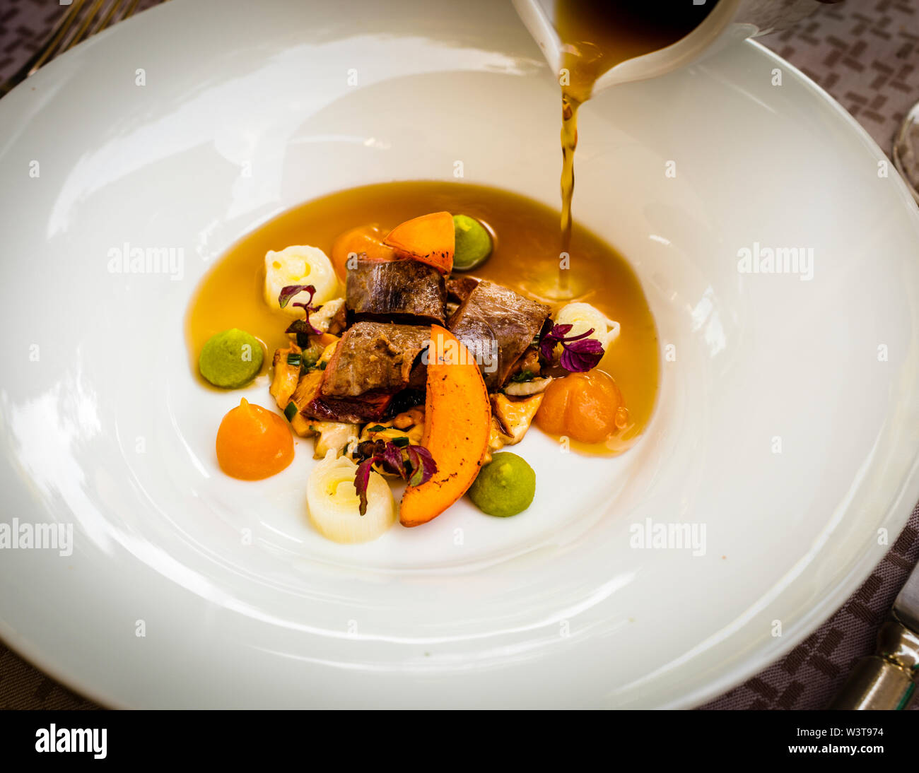 Piatto di Stella Michelin cucina Chef Frederik Desch di Laudensacks Ristorante, Bad Kissingen, Germania. Un fungo selvaggio boullion è versato qui su una sella rosa arrostita di veleno, canterelle, albicocche e porri Foto Stock