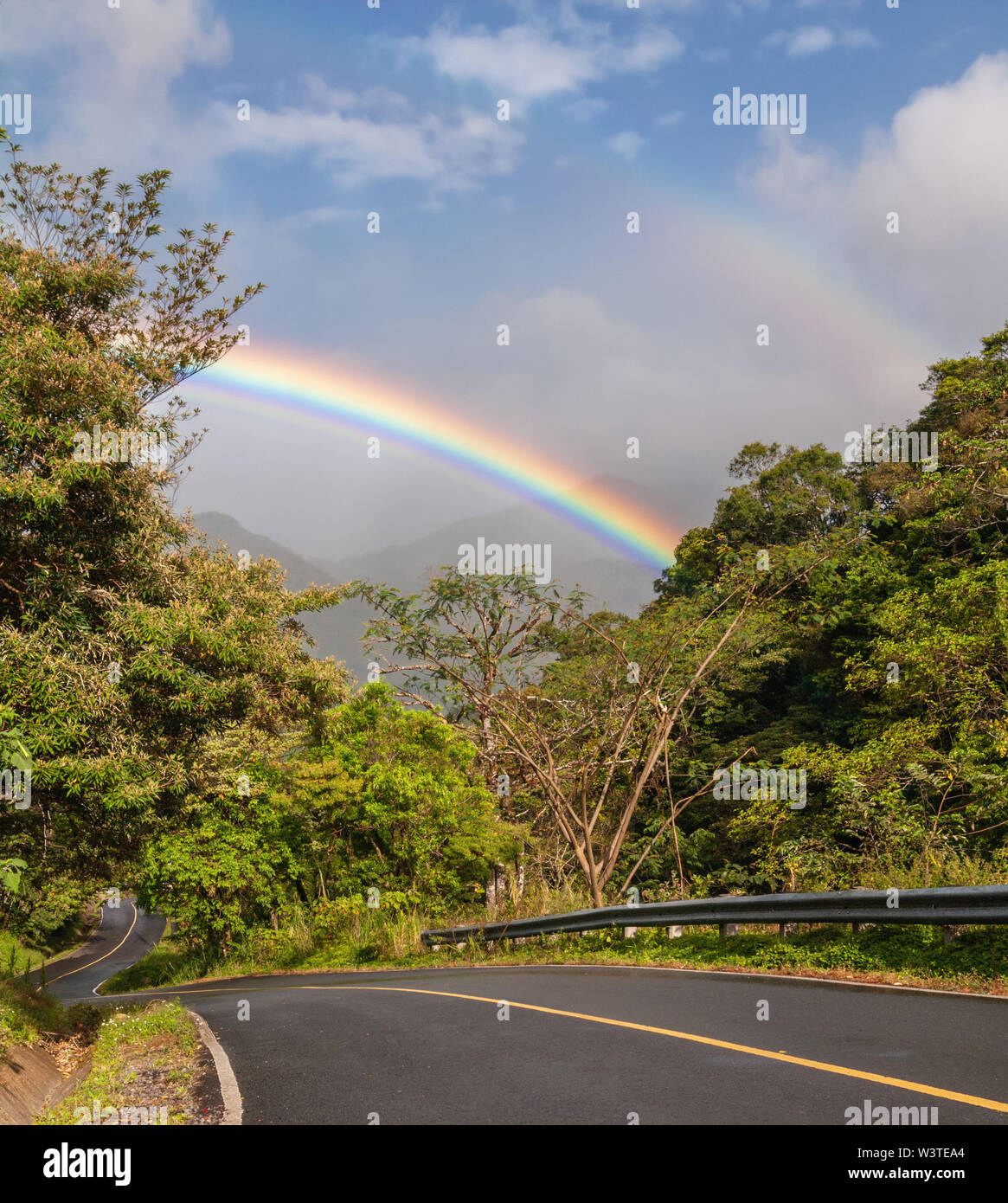 Intenso arcobaleno, una strada stretta tra una vegetazione lussureggiante mostrata a Boquete, una città negli altopiani del Panama occidentale. Foto Stock
