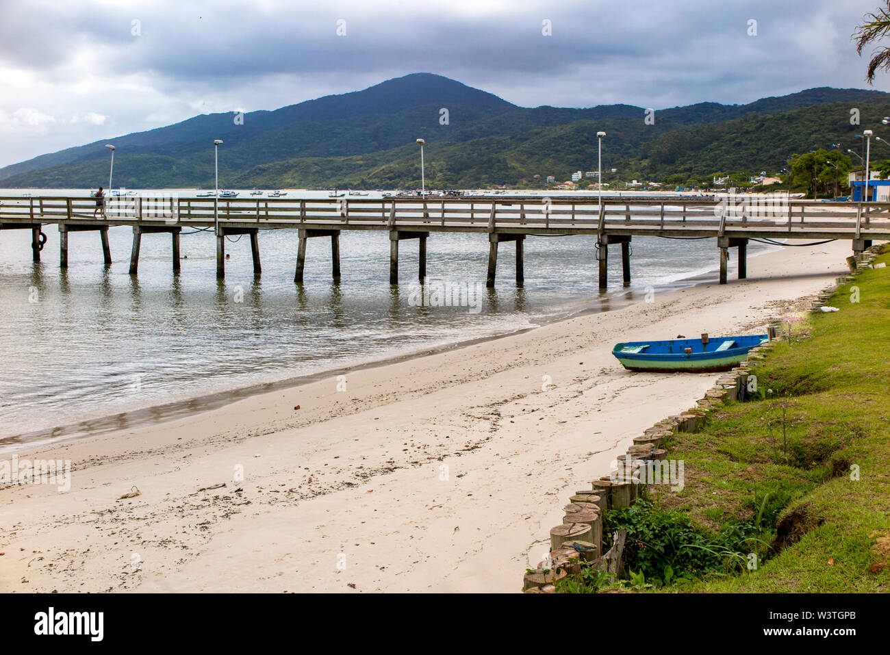 Dettaglio del molo in legno di Morrinhos beach, con legno barca da pesca e Zimbros beach in background, Bombinhas, Santa Catarina Foto Stock