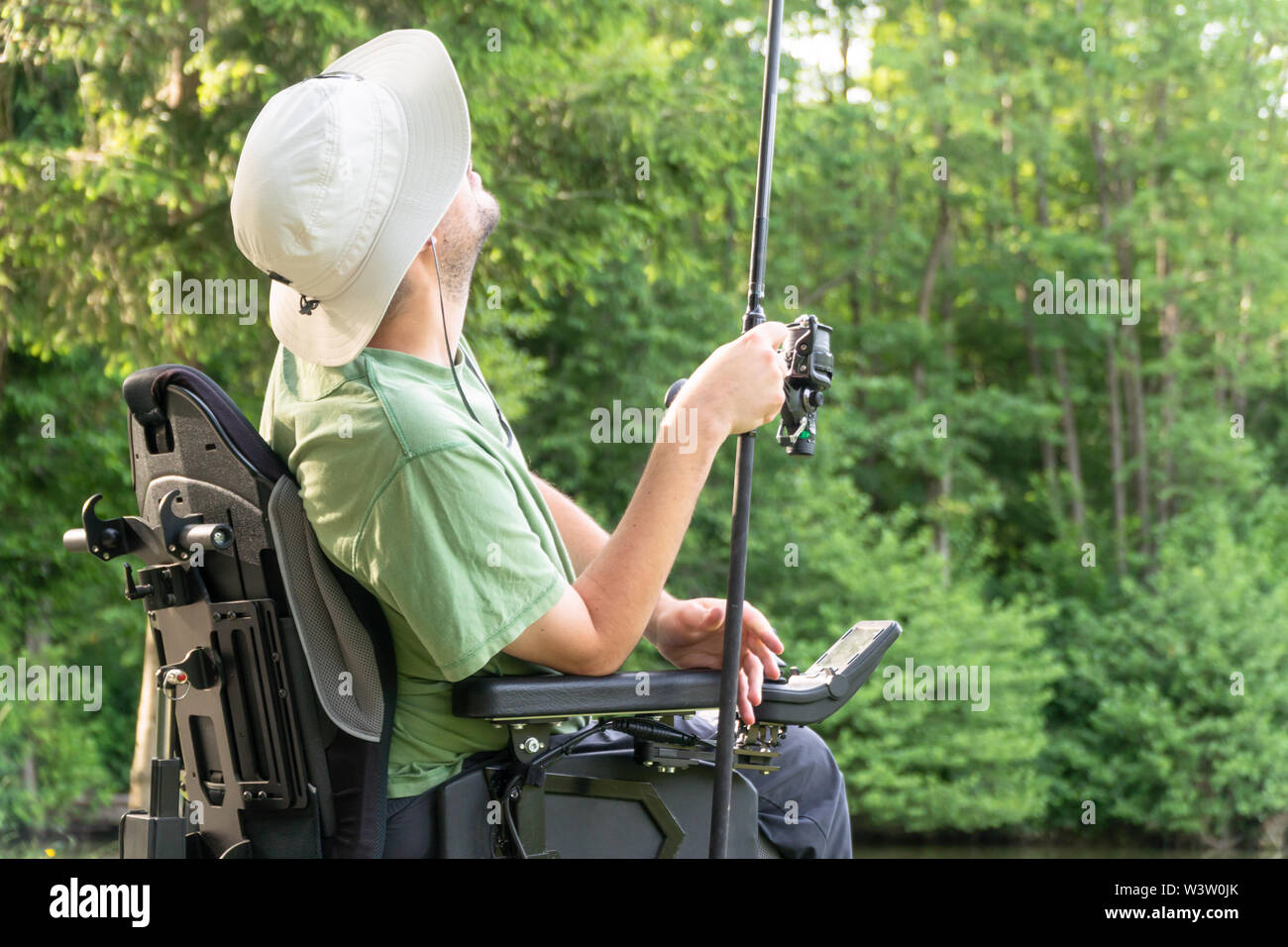 Uomo felice in una sedia elettrica gettando pesca polo al bellissimo stagno in natue in una giornata di sole Foto Stock
