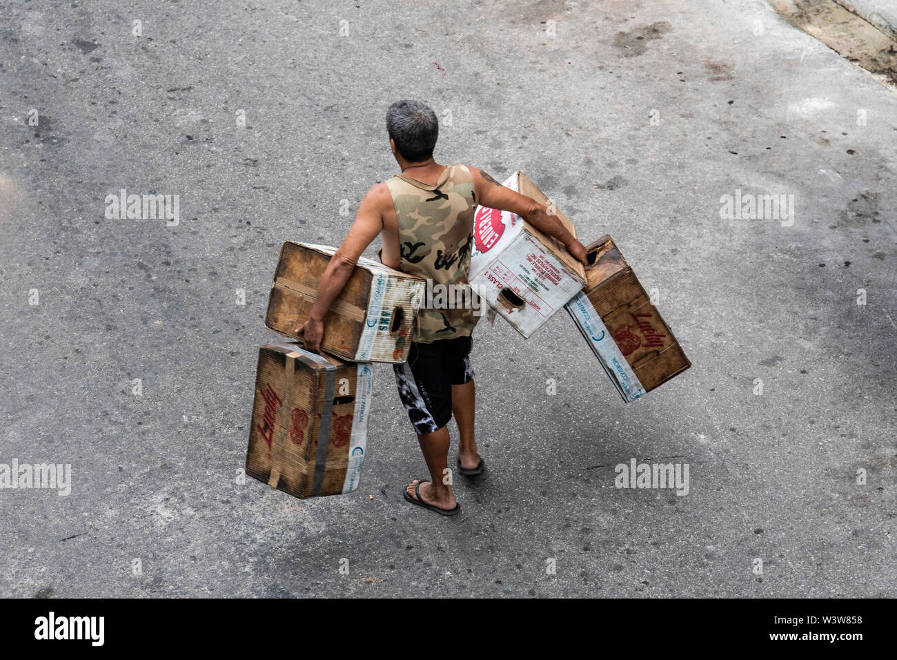 Un uomo che trasportava scatole e cassette cammina per la strada a l'Avana, Cuba Foto Stock