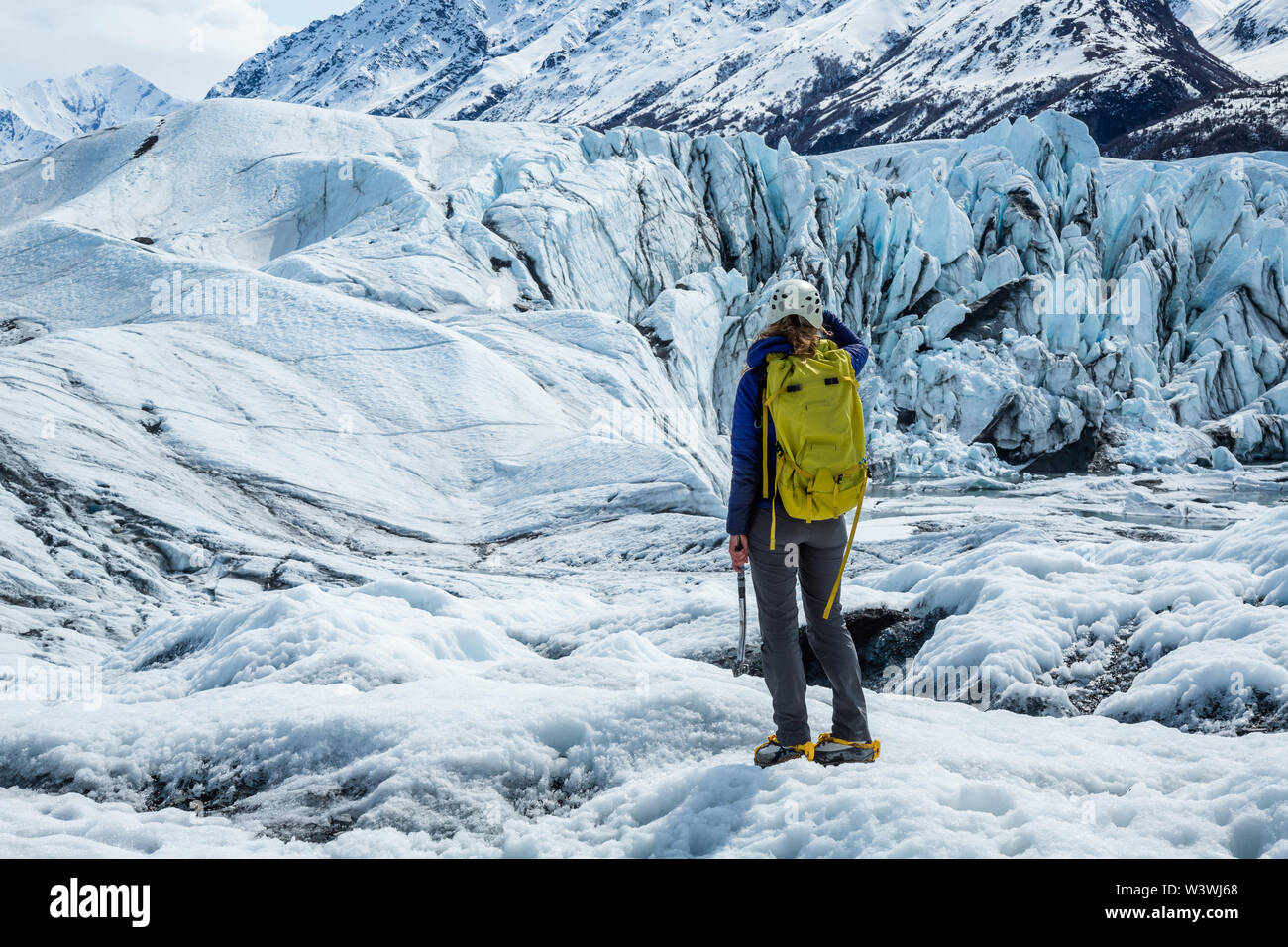 Giovane donna nel ghiacciaio ingranaggio di viaggio guardando verso un ghiacciaio del basso Matanuska Glacier in Alaska. Foto Stock