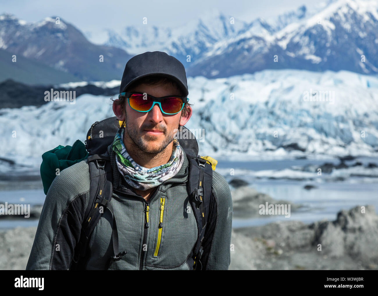 Un uomo in una sfera cappello e occhiali da sole con uno zaino sorge nella parte anteriore di un ghiacciaio in Alaska remoto. Egli è una guida, portare la gente fuori ghiaccio salire su una gl Foto Stock