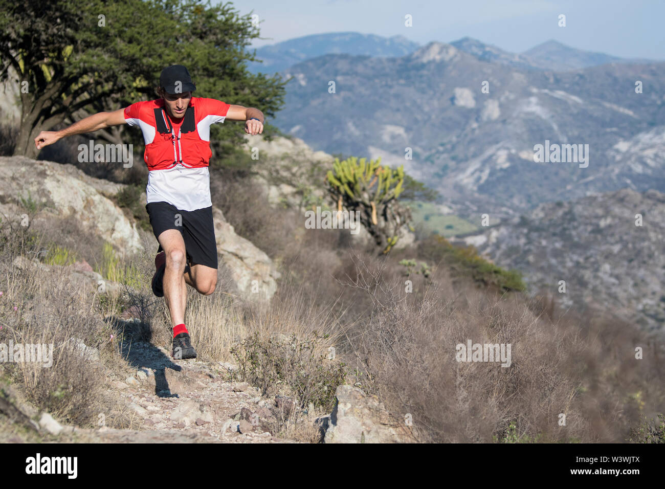 Un agile uomo di mezza età che indossa un cappello nero salta sopra una roccia mentre egli esplora i sentieri desertico delle Montagne di El Arenal, hidalgo, Messico. Foto Stock