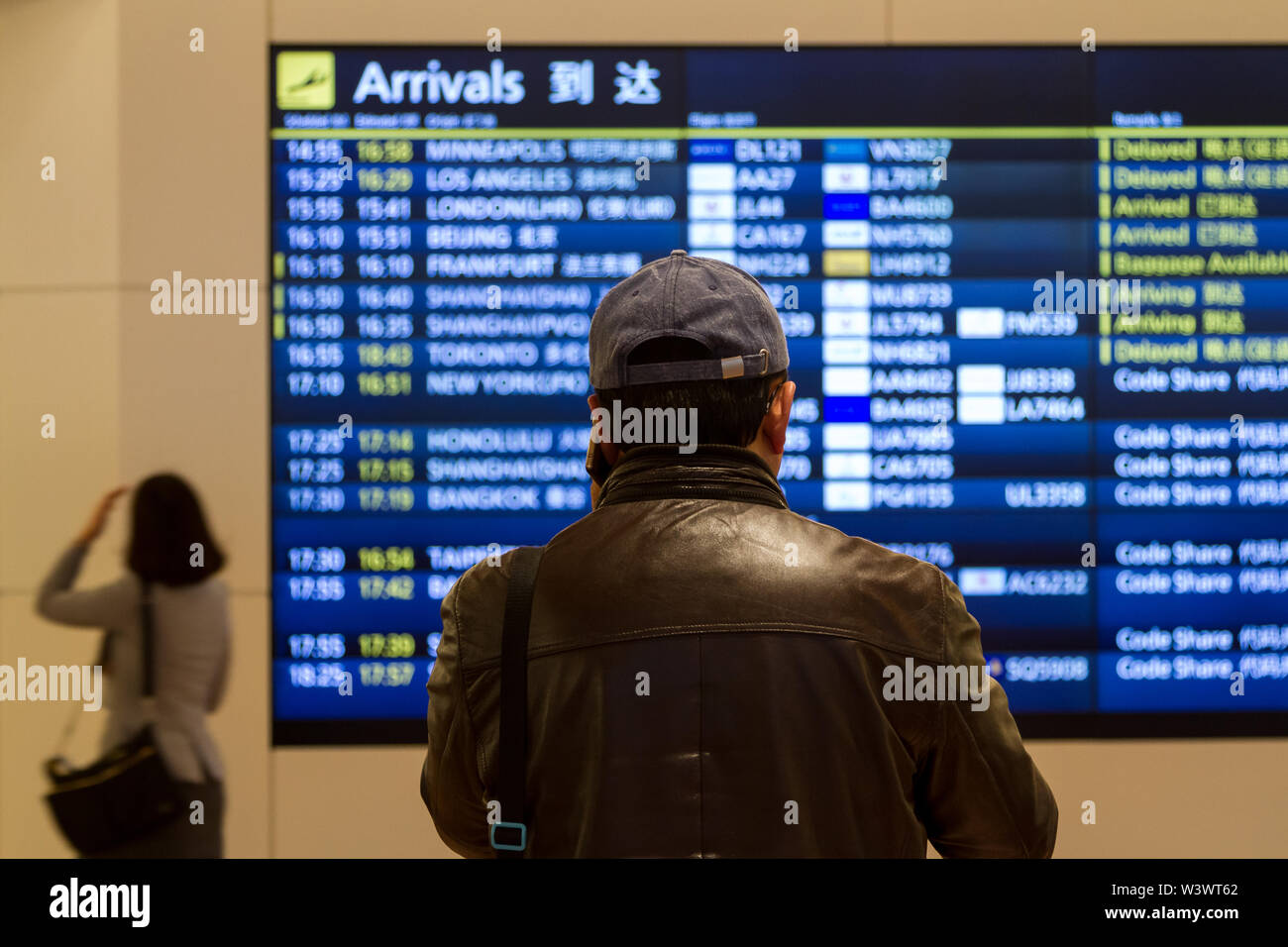 Un uomo in berretti da baseball guarda il Arrivals Board dell'aeroporto internazionale Haneda di Tokyo, Giappone. Foto Stock