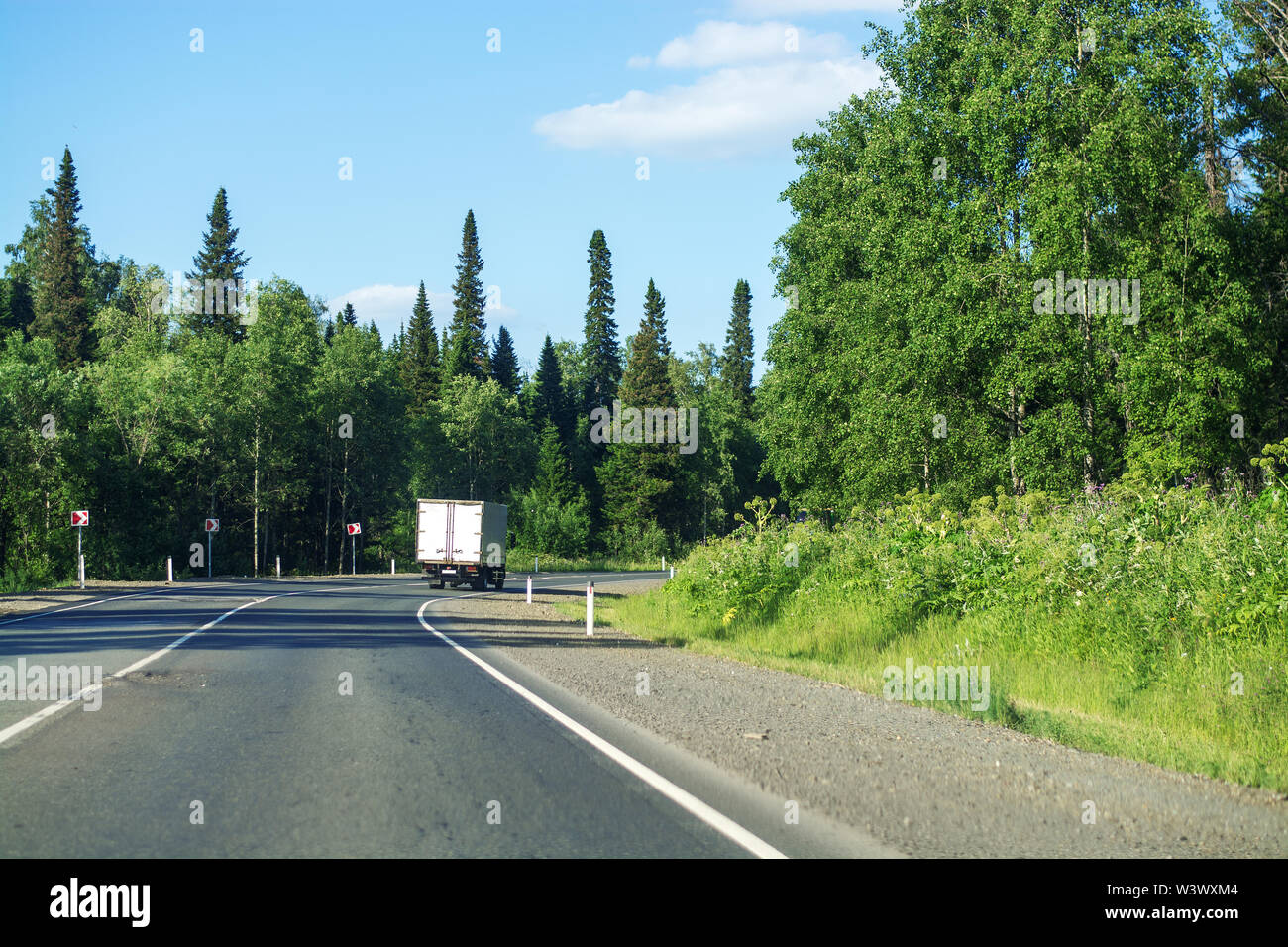 Strada asfaltata attraversando il bosco in una giornata di sole. In curva, cielo blu chiaro con cirrus nuvole bianche. Viaggio attraverso la Siberia Foto Stock