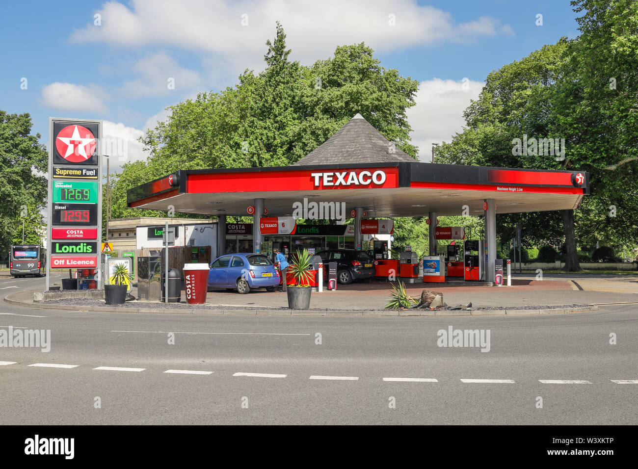 Texaco garage stazione di benzina che mostra la benzina e il gasolio i prezzi con la giovane donna riempie la sua automobile Foto Stock