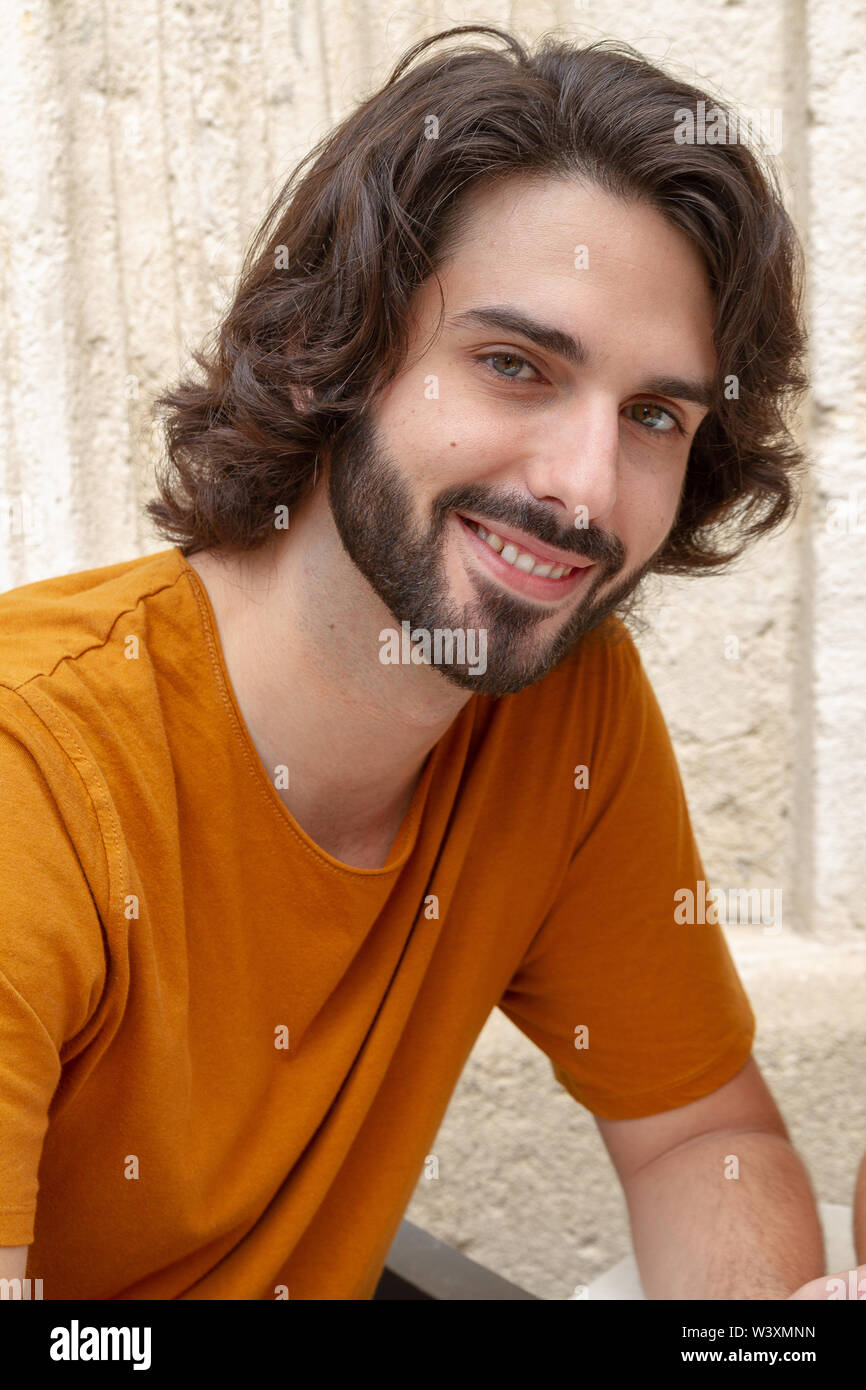 Ritratti di un giovane uomo sulla strada, guardando la fotocamera mentre il sorriso con una t-shirt arancione Foto Stock