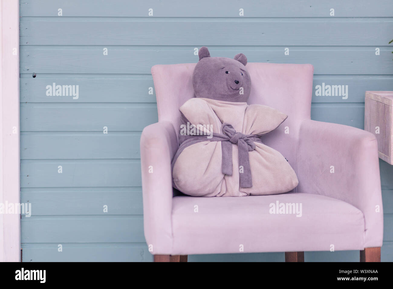 Cuscino nella forma di un orso su una morbida poltrona di colore viola che si erge contro una parete in legno Foto Stock