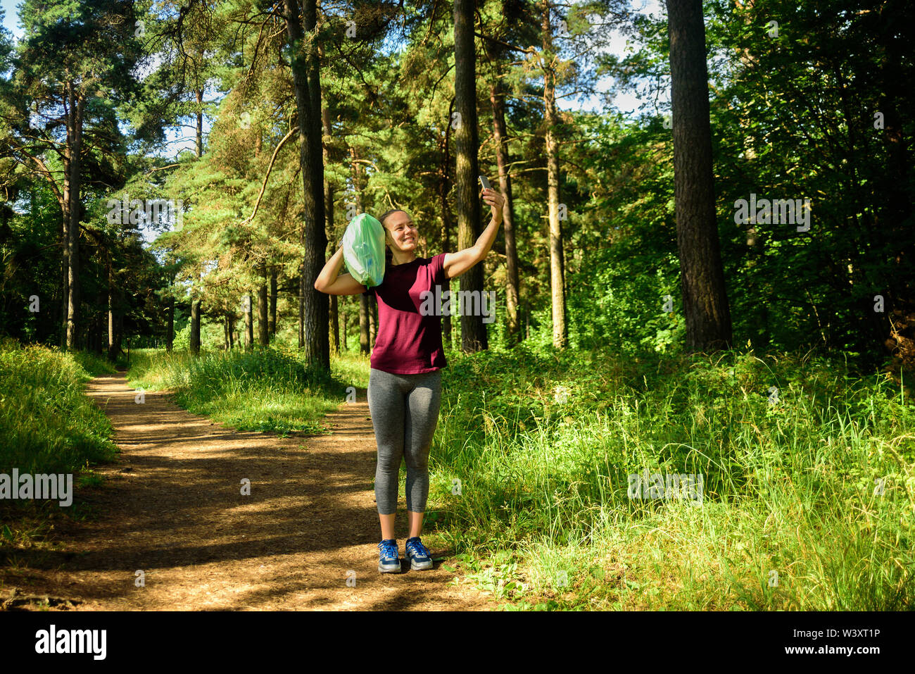 Donna prendendo foto con garbage bag in foresta. Dopo la raccolta il cestino a fare jogging. Concetto Plogging Foto Stock