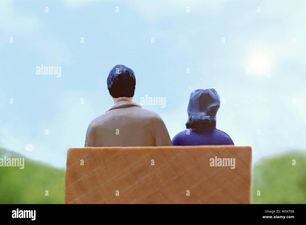 Vista posteriore di un uomo e di una donna seduta su una panchina guardando ottimista verso il futuro, simbolico foto con statuine in miniatura Foto Stock