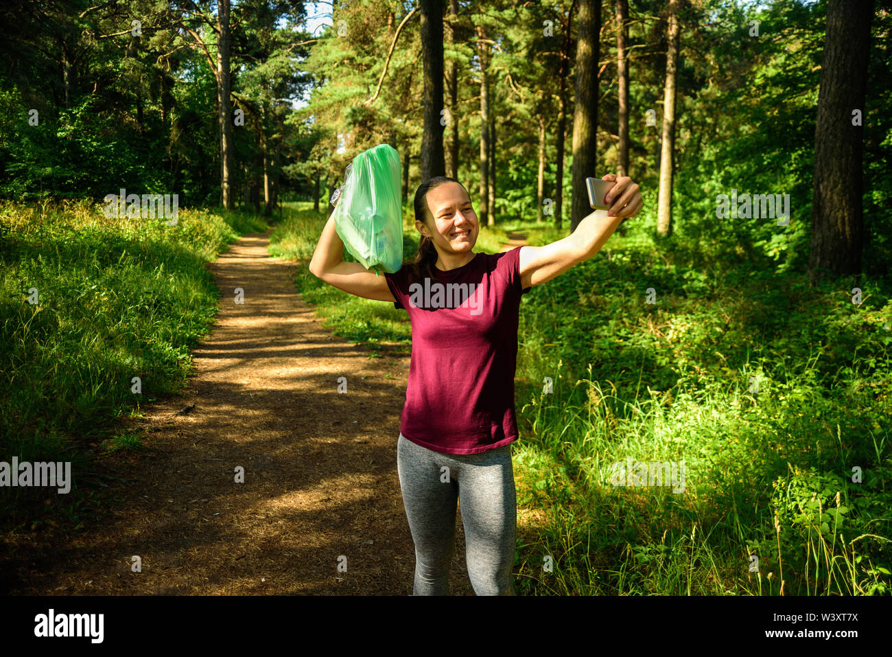 Donna prendendo foto con garbage bag in foresta. Dopo la raccolta il cestino a fare jogging. Concetto Plogging Foto Stock