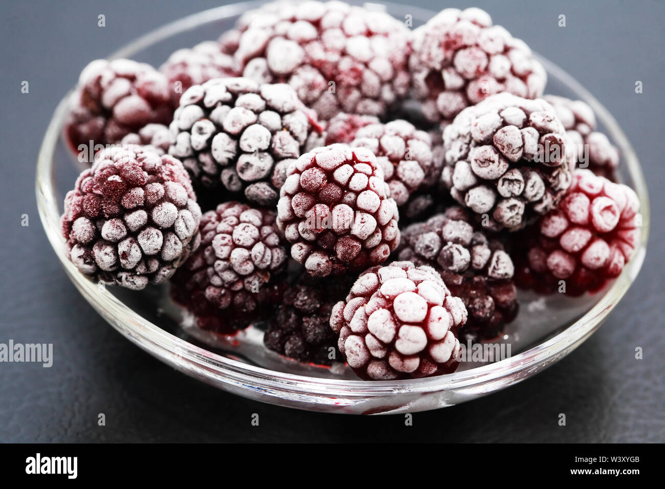 Piattino con il mucchio di congelati frutti neri su sfondo scuro Foto Stock