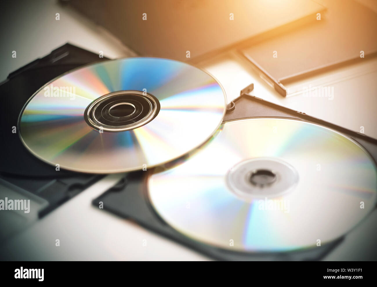 Due CD per la riproduzione di musica e video e informazioni di registrazione che sono ora meno utilizzati fuori uso, giacciono su un tavolo bianco, illuminato dalla luce del sole. Foto Stock