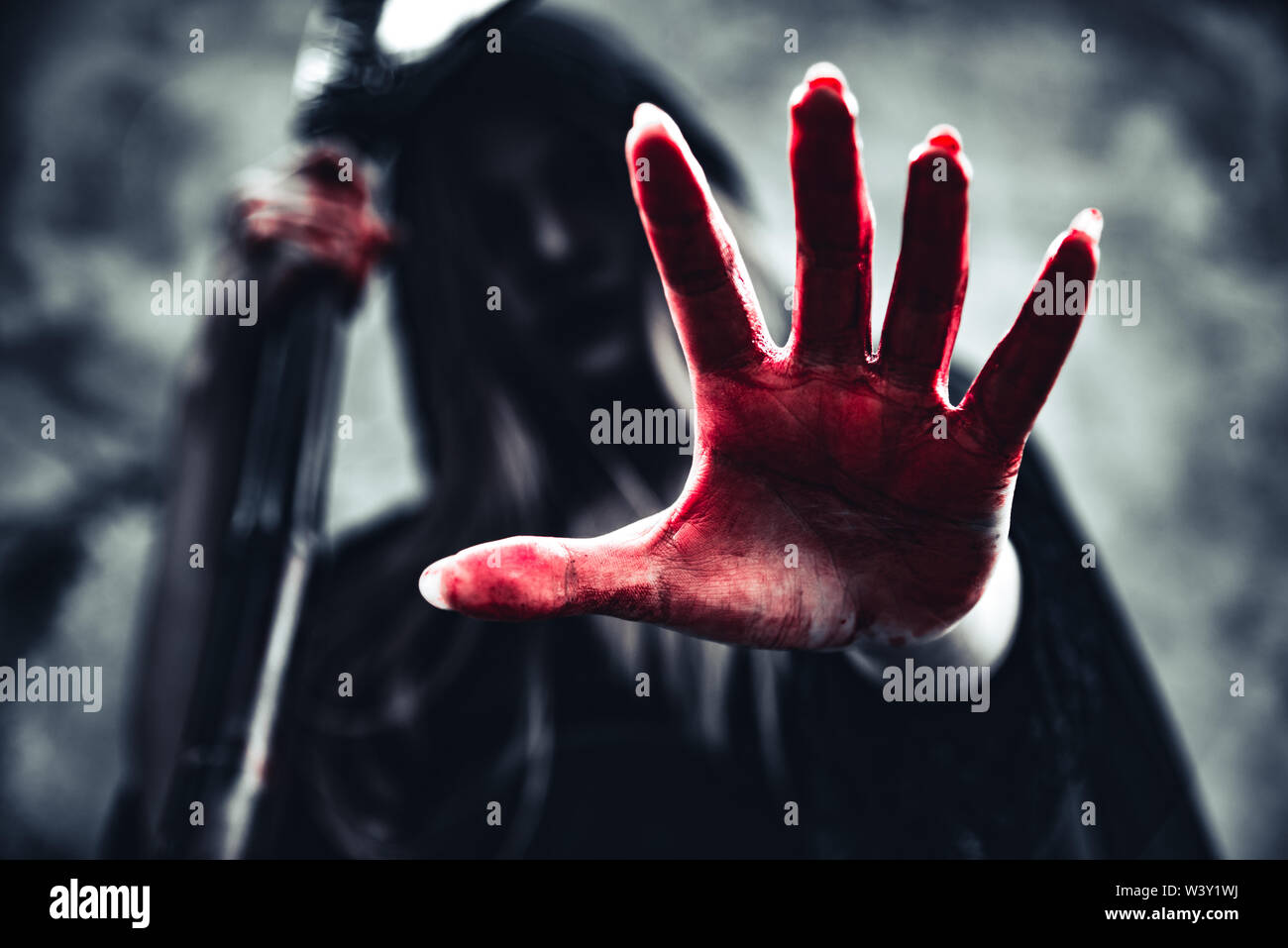 Strega che mostra sanguinosa mano con reaper. Demone femminile angelo vestiti di nero e il cofano sulla parete grunge background. Il giorno di Halloween e il mistero del concetto. Fant Foto Stock