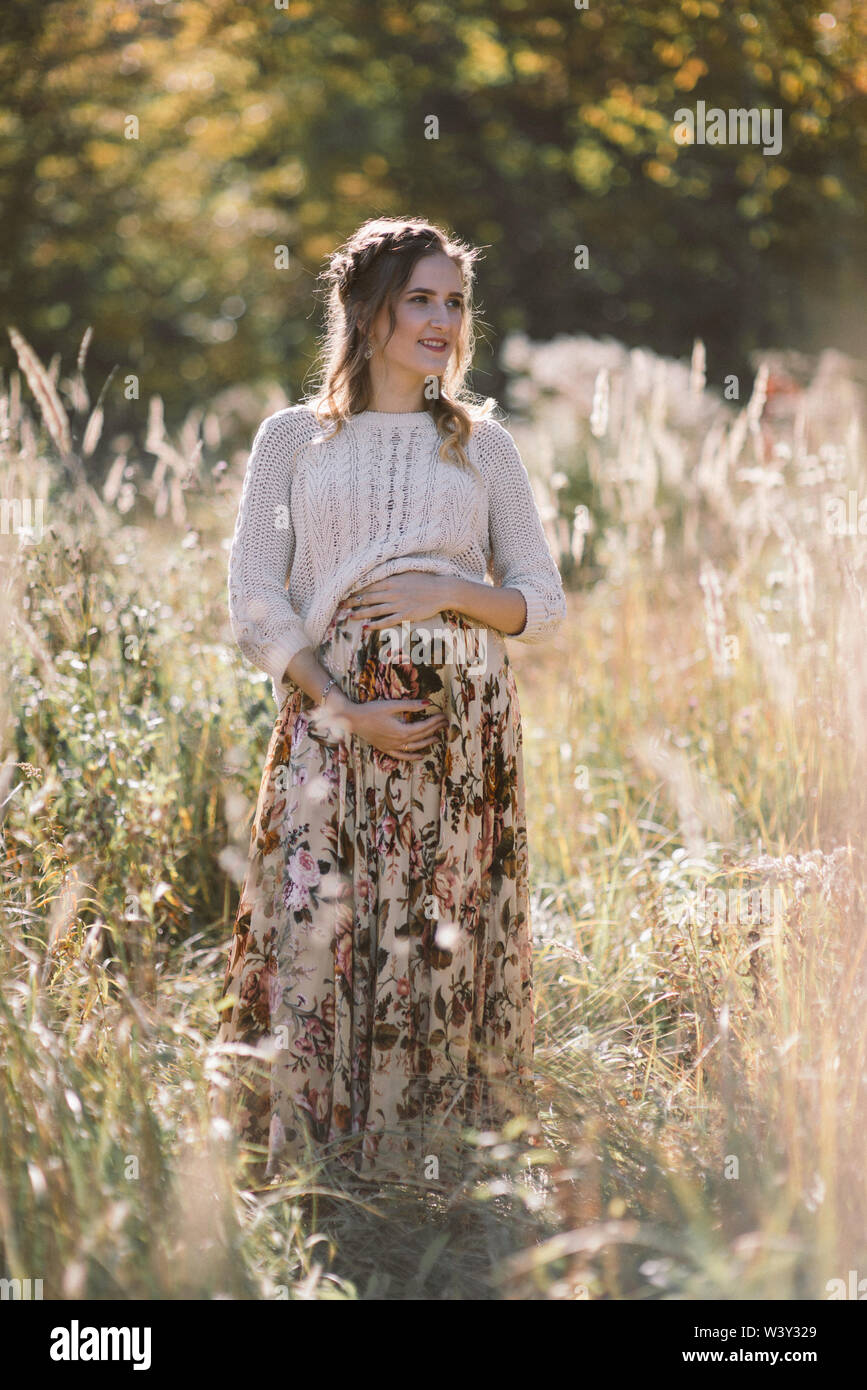 Ritratto di giovane donna in stato di gravidanza nel campo d'autunno. Foto Stock