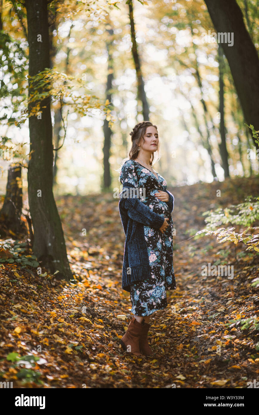 Trasognata donna incinta con gli occhi chiusi nella foresta di autunno. Foto Stock