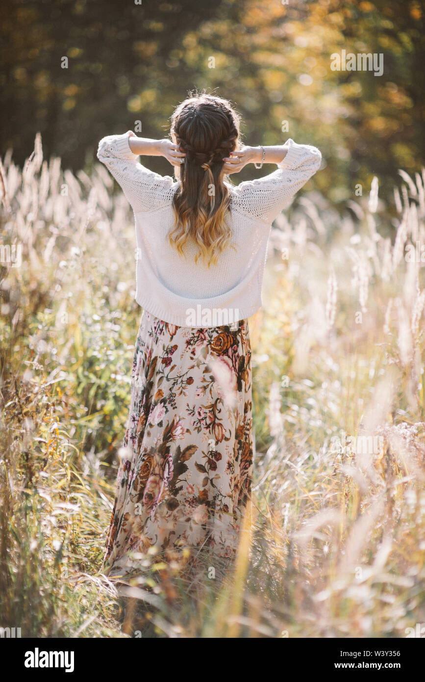 Vista posteriore del giovane romantico capelli lunghi donna in maglia bianca sul campo d'autunno. Foto Stock