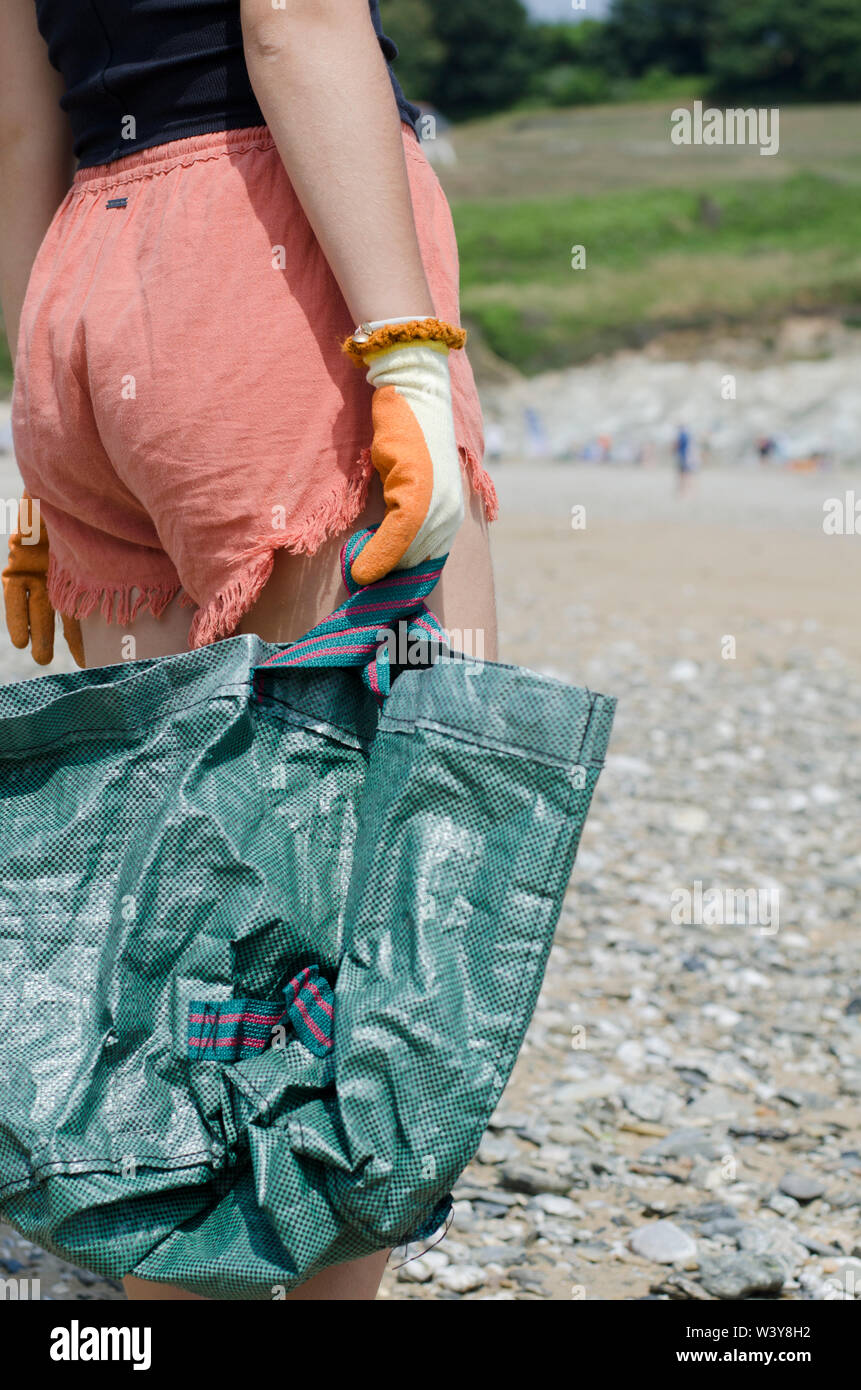 Mani guantate azienda verde sacchetto di plastica sulla spiaggia Foto Stock