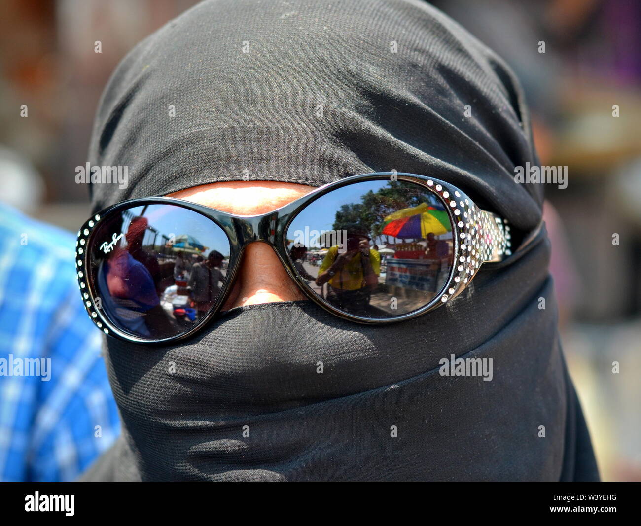 Completamente coperta Muslima indiano indossa un niqab nero e nasconde i suoi occhi dietro gli occhiali da sole con mirroring. Foto Stock