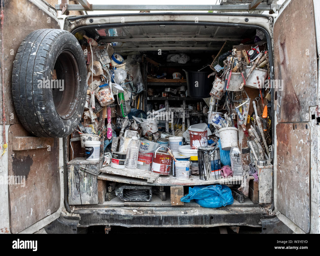 Interno di una casa del decoratore van fotografata dalla parte posteriore, pieno di vecchi barattoli di vernice, accessori, pennelli e altri materiali di consumo Foto Stock