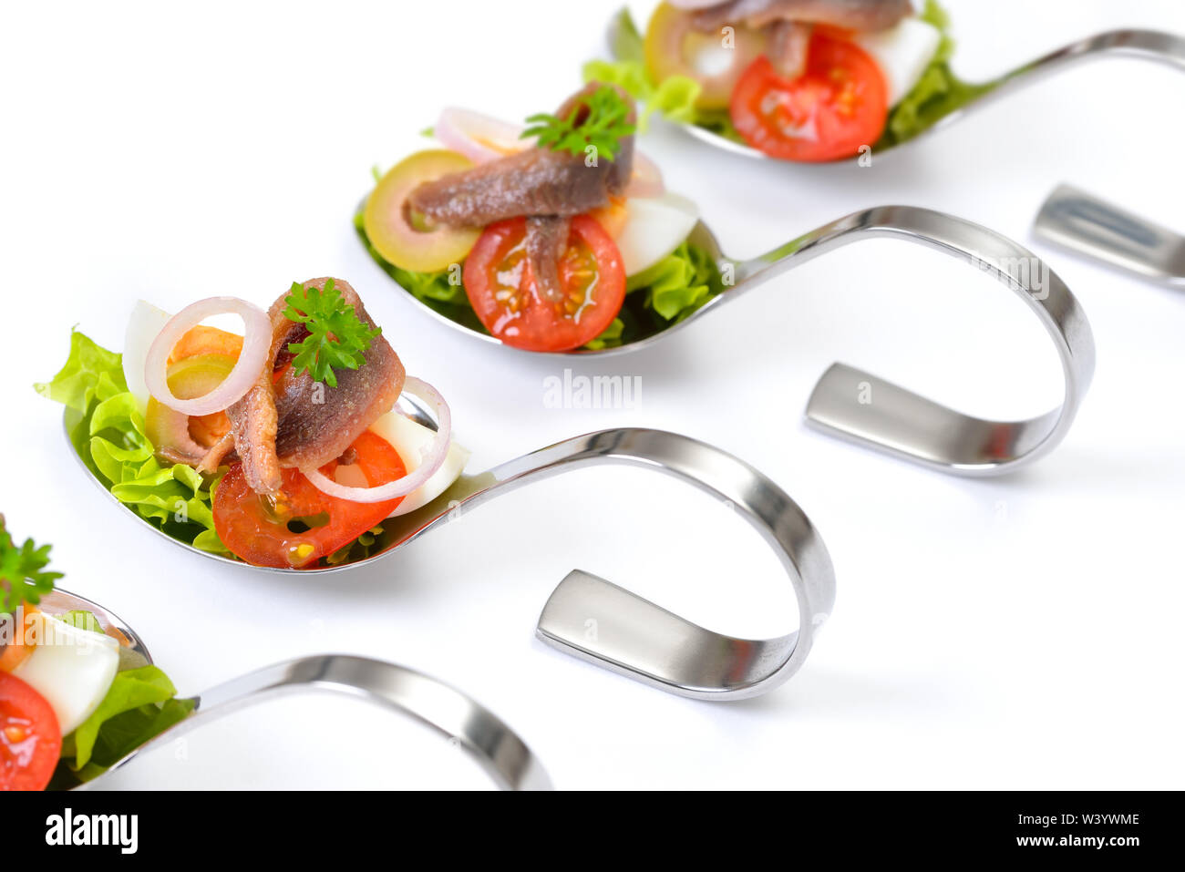 Raffinati antipasti di pesce con i filetti di acciuga e uova a servire i cucchiai collocati su uno sfondo bianco Foto Stock