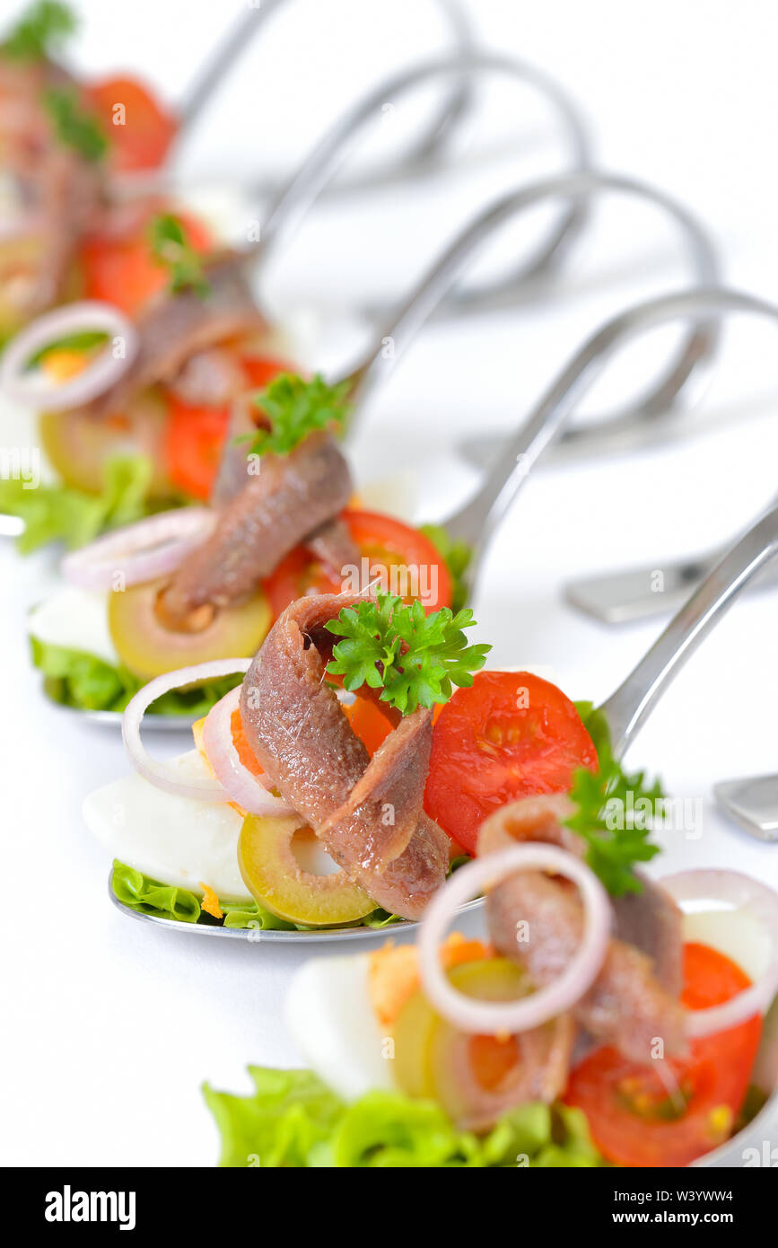 Raffinati antipasti di pesce con i filetti di acciuga e uova a servire i cucchiai collocati su uno sfondo bianco Foto Stock