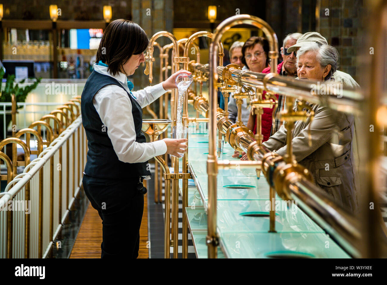 Un addetto alla fontana versa acqua curativa per un ospite del spa prima del concerto pomeridiano all'interno dell'edificio del spa di Bad Kissingen, Germania. In questo rituale di lunga data, agli ospiti viene versata acqua durante il concerto; ha appena un sapore piacevole, ma viene sorseggiata lentamente e senza fretta. L'orchestra da salotto suona nella sala ornata, che ha stabilito un record mondiale Guinness con 727 concerti solo nel 2016. Foto Stock