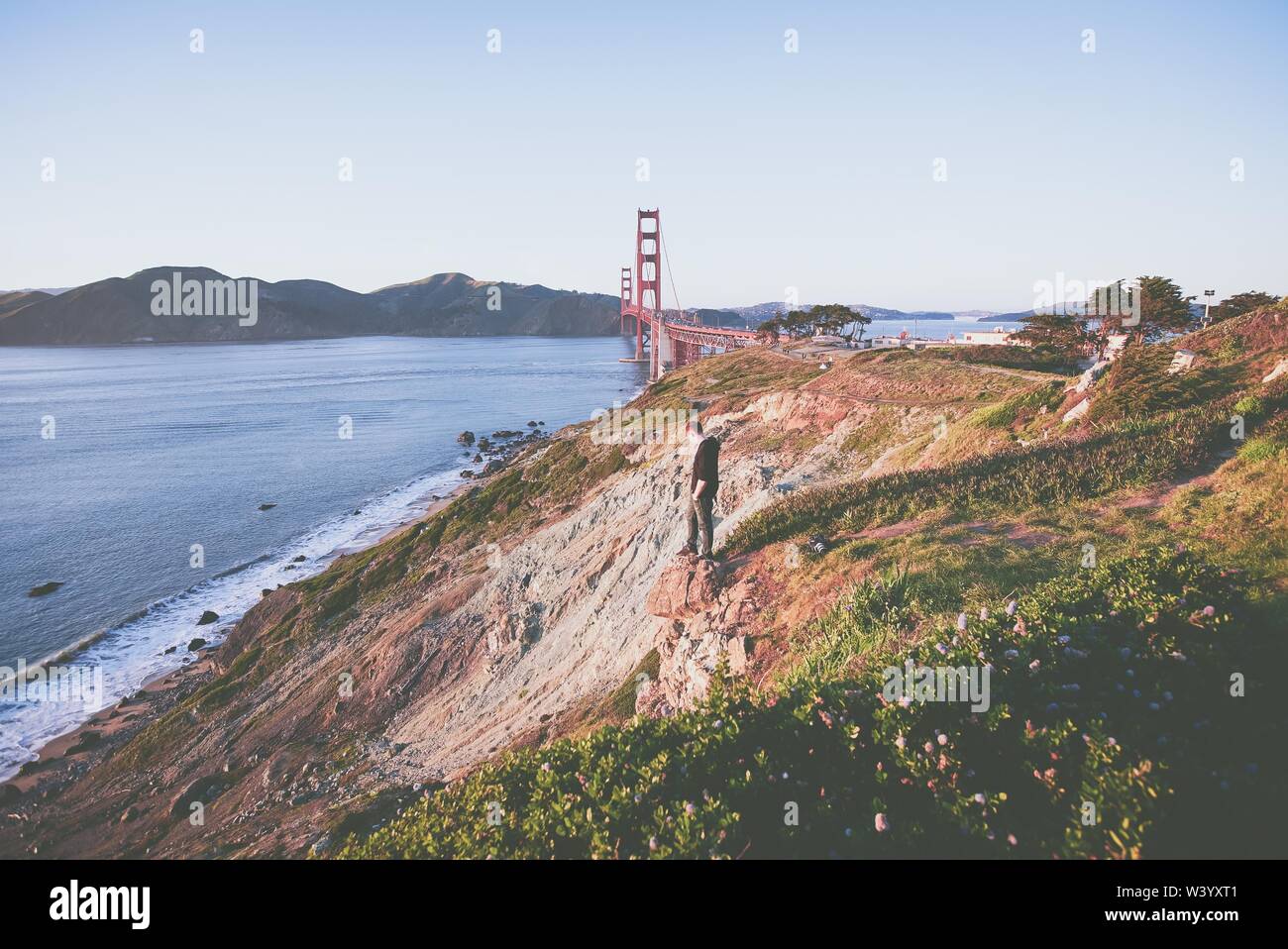 Maschio in piedi su una scogliera che guarda in basso vicino al mare E il ponte Golden Gate Foto Stock