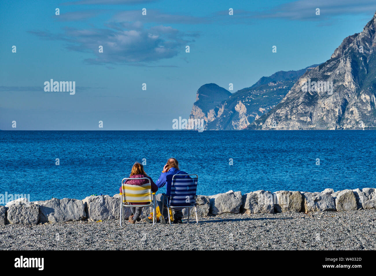Turisti che si siedono sulla spiaggia a piccolo porto Porticcioloat Lago di Garda, il Lago di Garda in Torbole - Nago, Riva, Trentino , Italia al 15 aprile 2019. © P Foto Stock
