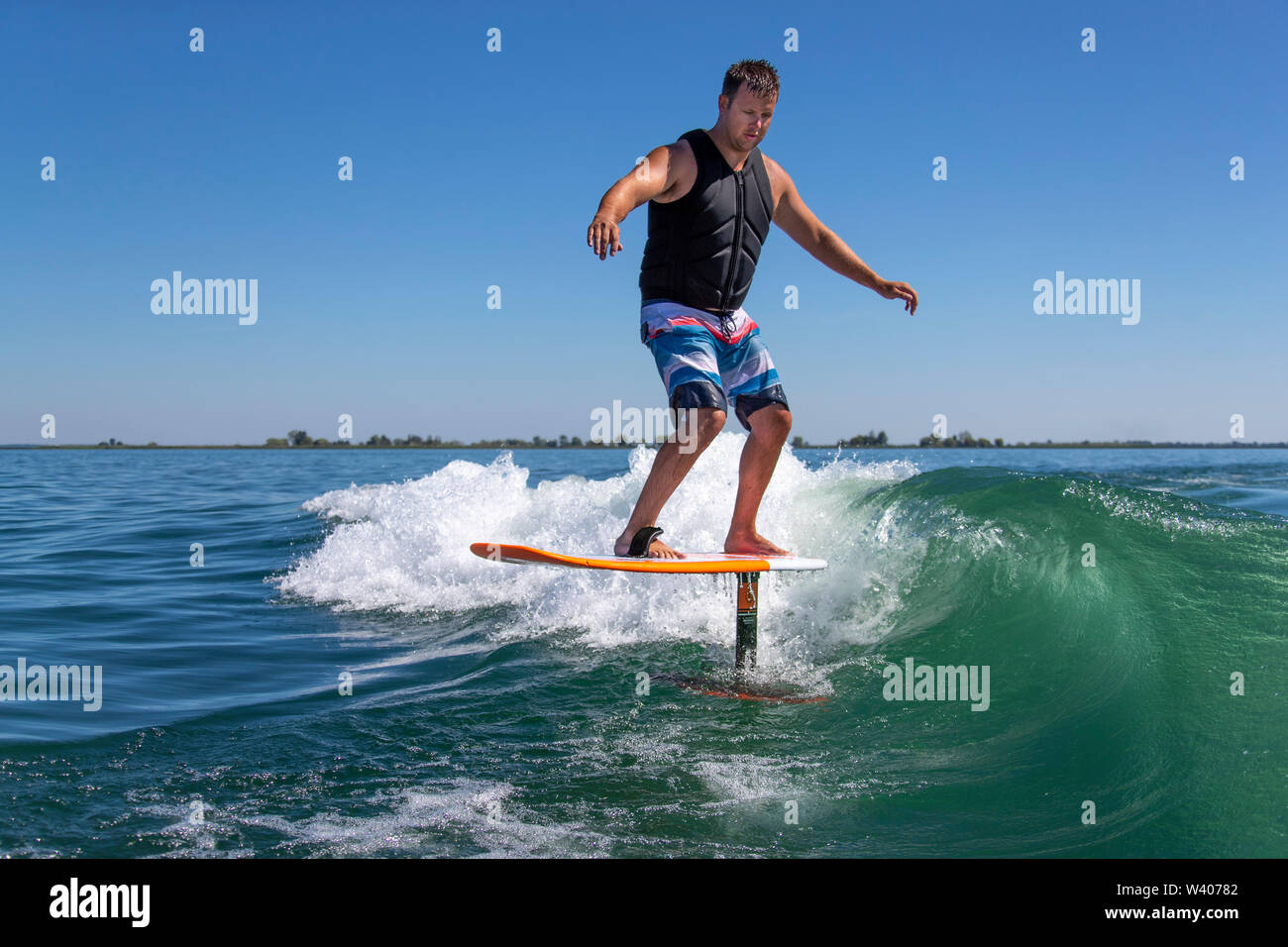 Un uomo su una lamina bordo navigando su una barca in scia. Foto Stock