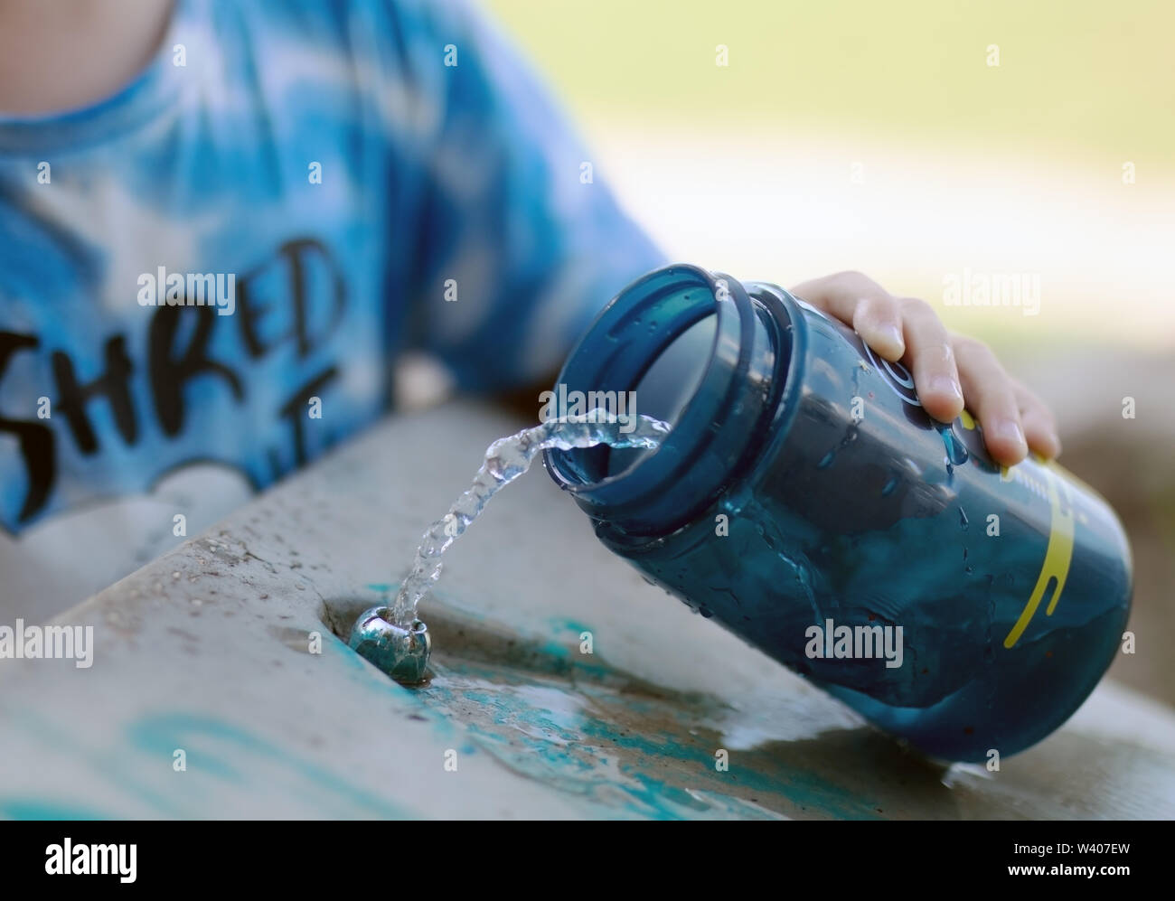 Bambino con una bottiglia di acqua potabile vicino lo scambiatore di calore nel parco raccoglie acqua fredda per rinfrescarvi dal caldo estivo Foto Stock