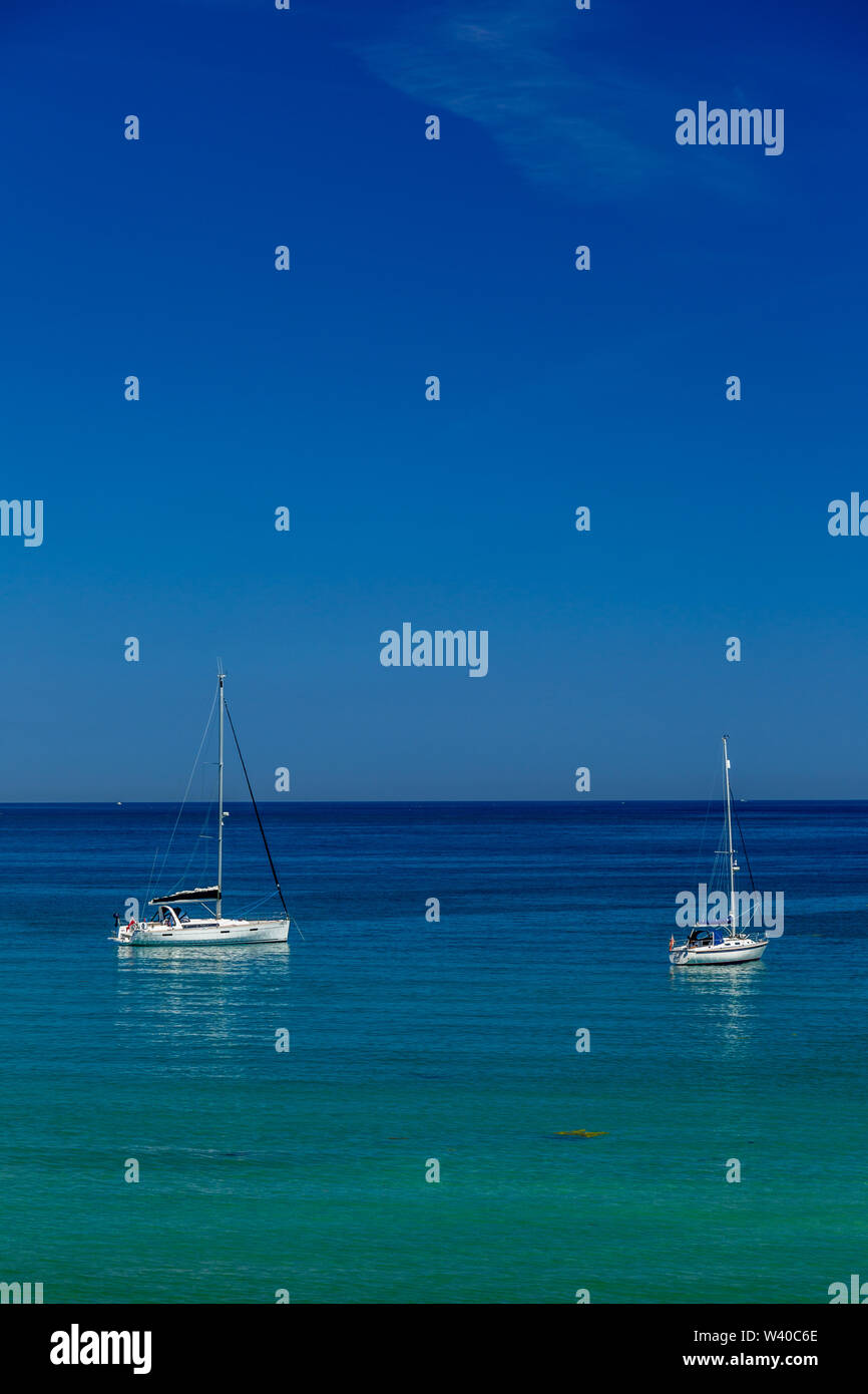 Due yacht ormeggiati al largo della costa della Cornovaglia, Inghilterra. Il mare è molto blu e appare quasi tropicale. Foto Stock