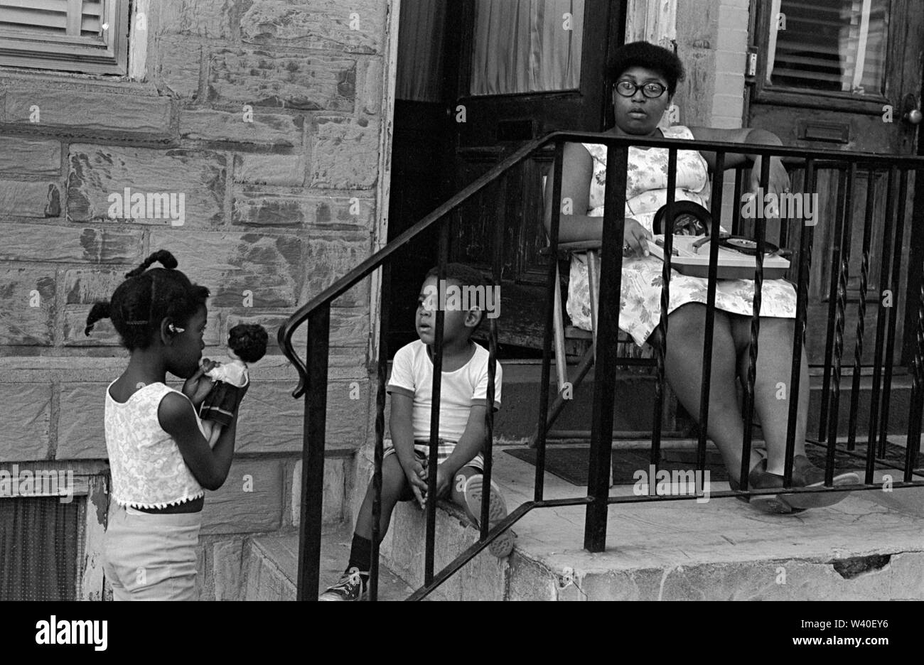 Madre e figli afroamericani degli anni '1960, la ragazza sta giocando con una bambola bianca con capelli ricci neri. La madre sta ascoltando la musica su un lettore di registrazione portatile ha al suo giro alcuni dischi singoli e dischi a 45 giri/min. Sono sul portico della loro casa. New Brunswick, New Jersey, 1969, USA 60s US HOMER SYKES Foto Stock
