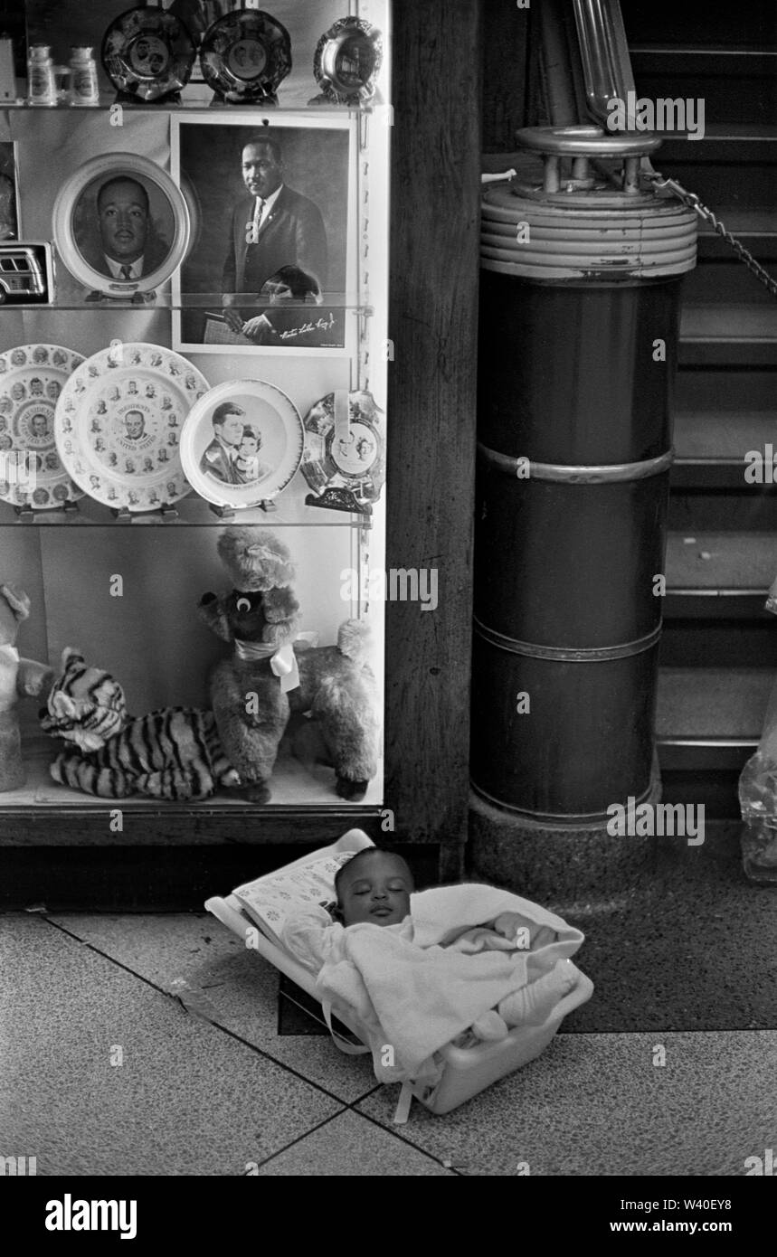 African bambino americano degli anni sessanta nella culla portatile collocato sul pavimento sotto Negozio di souvenir di Martin Luther King e il Kennedy in una stazione degli autobus Greyhound. Atlanta, Georgia 1969, STATI UNITI D'AMERICA 60s NOI HOMER SYKES Foto Stock