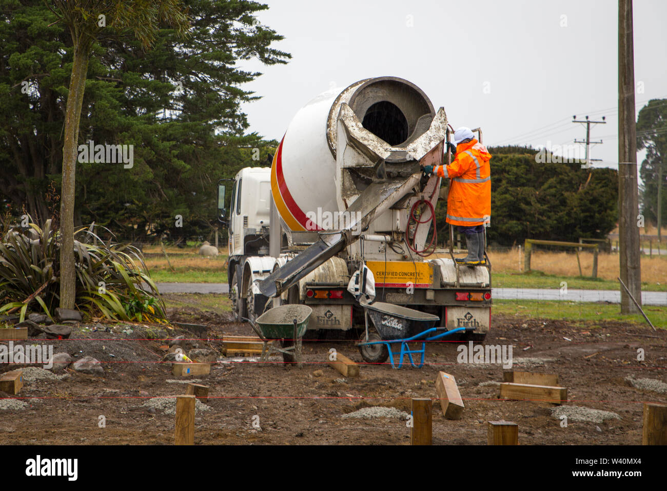 Annat, Canterbury, Nuova Zelanda, 19 Luglio 2019: Costruttori Cariola di cemento bagnato da un mescolatore concreto carrello per pali di fondazione in un edificio rurale sit Foto Stock