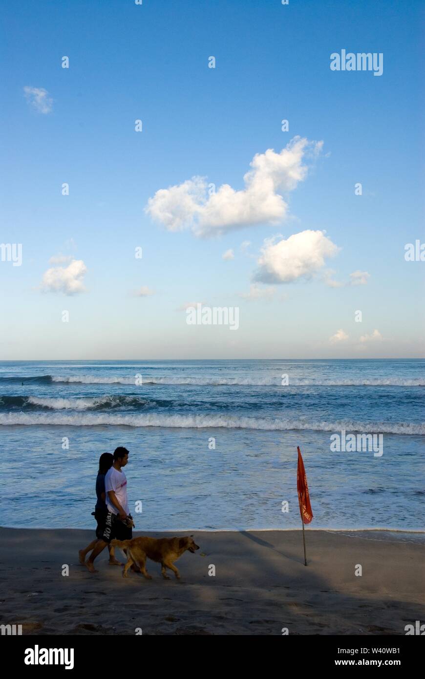 La spiaggia di Kuta Beach, Bali, Indonesia - Giugno 2019 : la gente a piedi con un cane su una spiaggia con un contrassegno di sicurezza. Foto Stock
