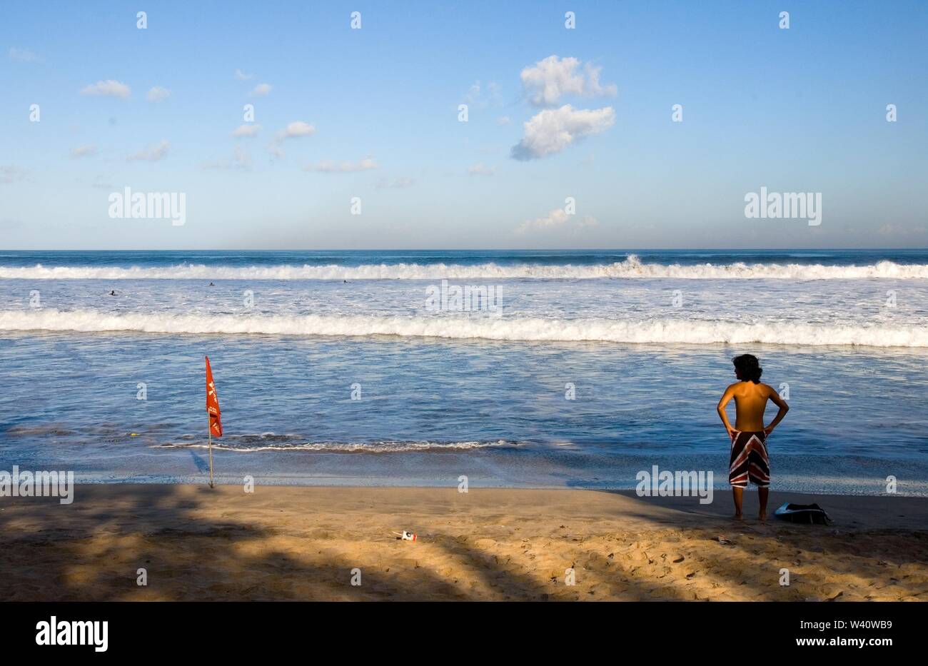 La spiaggia di Kuta Beach, Bali, Indonesia - Giugno 2019 : un surfista è controllare l'onda su una spiaggia con un contrassegno di sicurezza. Foto Stock