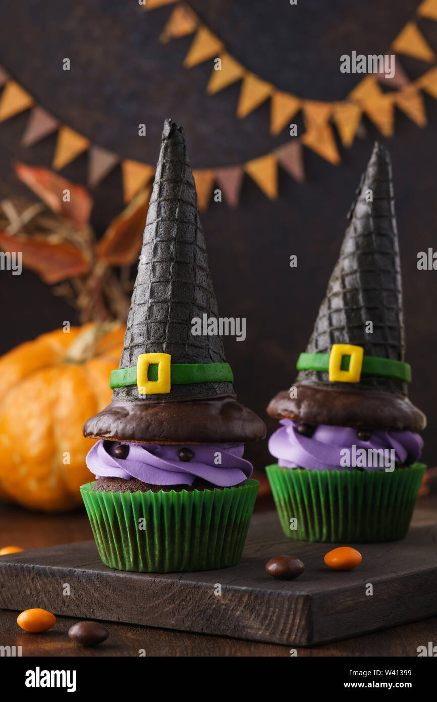 Halloween funny cupcake mostri con wafer cappelli di strega e caramelle per un partito. Festosa celebrazione i dolciumi e caramelle su sfondo di legno. Foto Stock