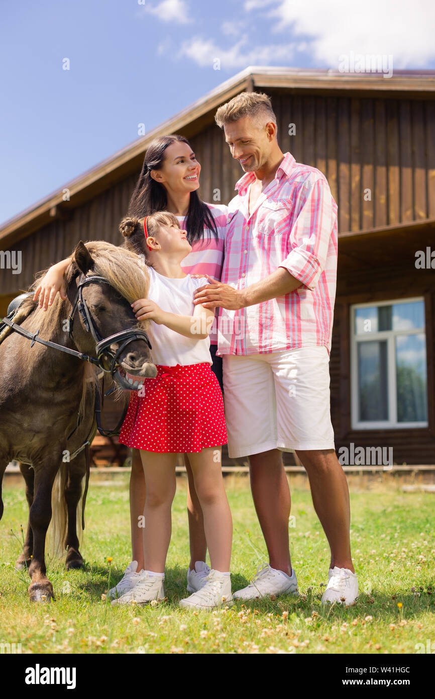 I genitori in piedi vicino a figlia toccando bel cavallo marrone Foto Stock