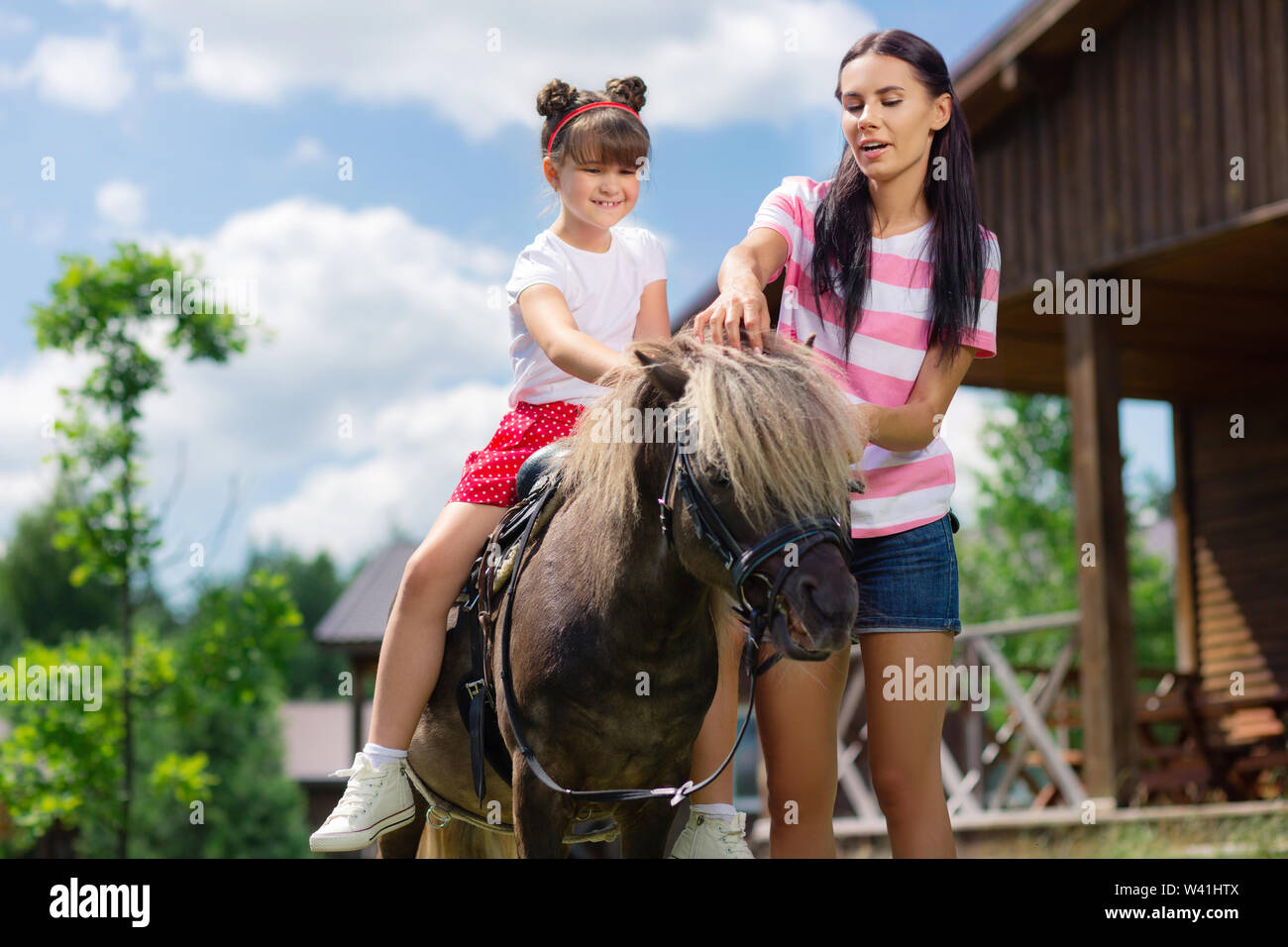 Ragazza dai capelli scuri godendo di equitazione con sua madre premurosa Foto Stock