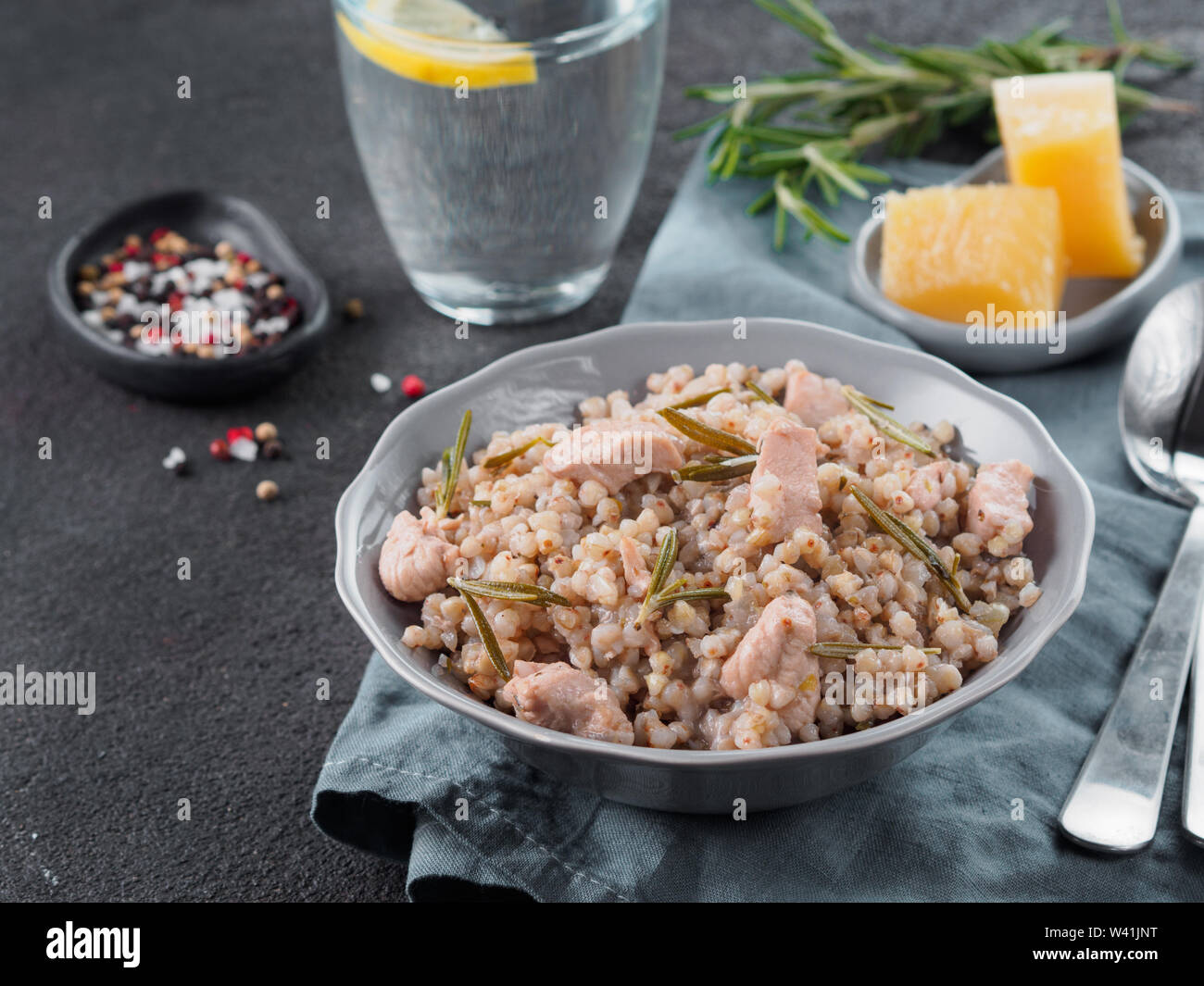 Materie del grano saraceno risotto con carne di pollo e il rosmarino servita parmigiano reggiano in lastra grigia su nero lo sfondo di cemento. Senza glutine e grano saraceno ricetta idee. Spazio di copia Foto Stock