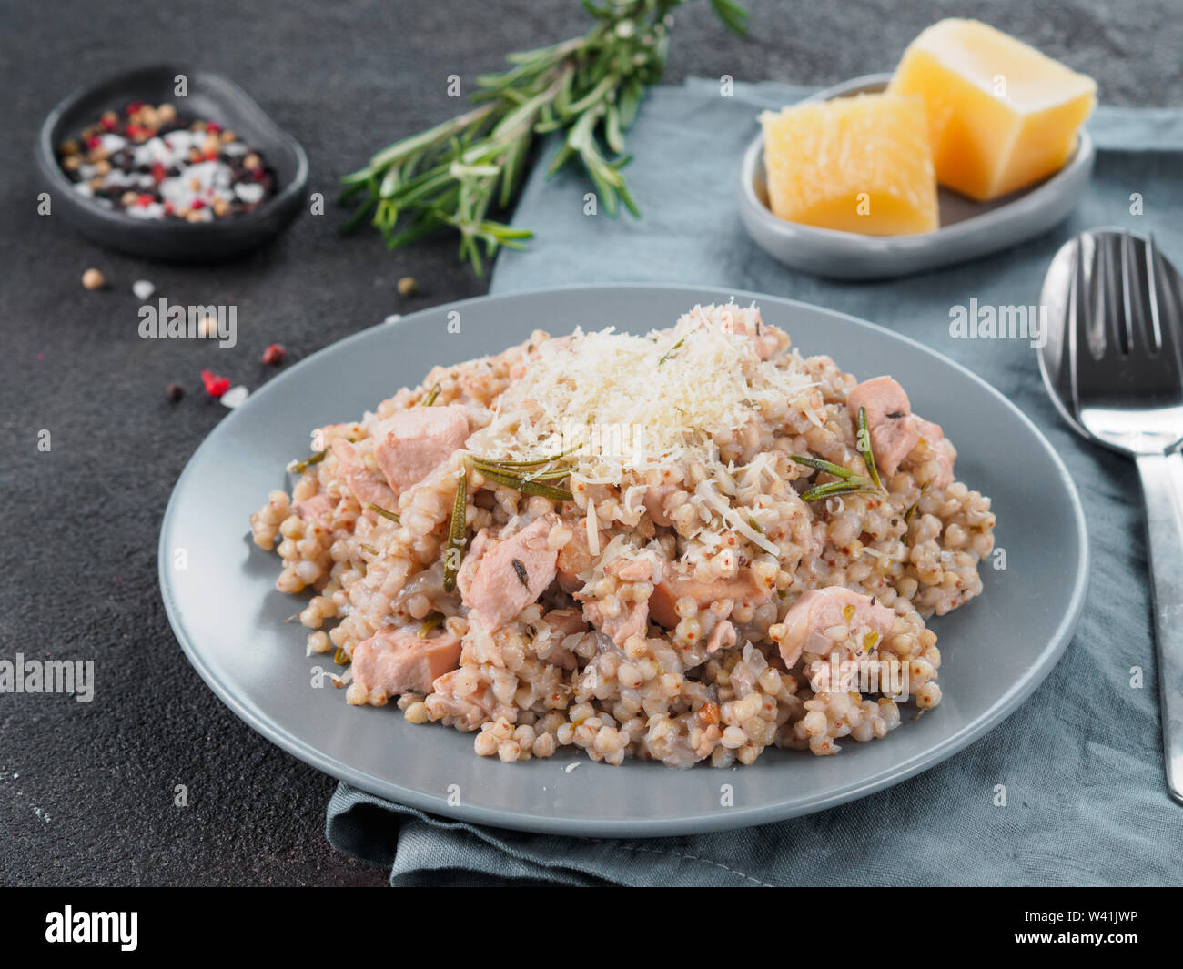 Materie del grano saraceno risotto con carne di pollo e il rosmarino servita parmigiano reggiano in lastra grigia su nero lo sfondo di cemento. Senza glutine e grano saraceno ricetta idee. Spazio di copia Foto Stock