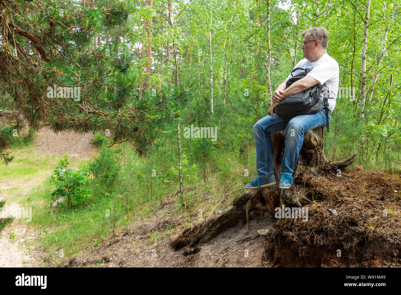 Un uomo seduto su un tronco di albero nella foresta Foto Stock