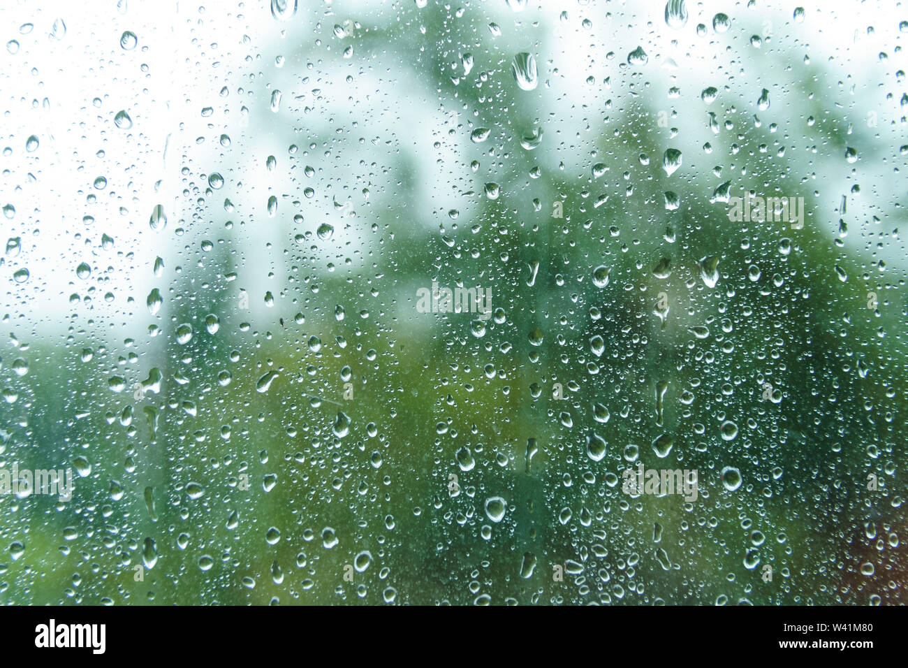 Gocce di pioggia sulla giornata piovosa su fuori di vetro con bordi sfocati. La pioggia al di fuori del riquadro della finestra nella giornata di primavera. Gocce di acqua di fluire in basso la superficie. Foto Stock