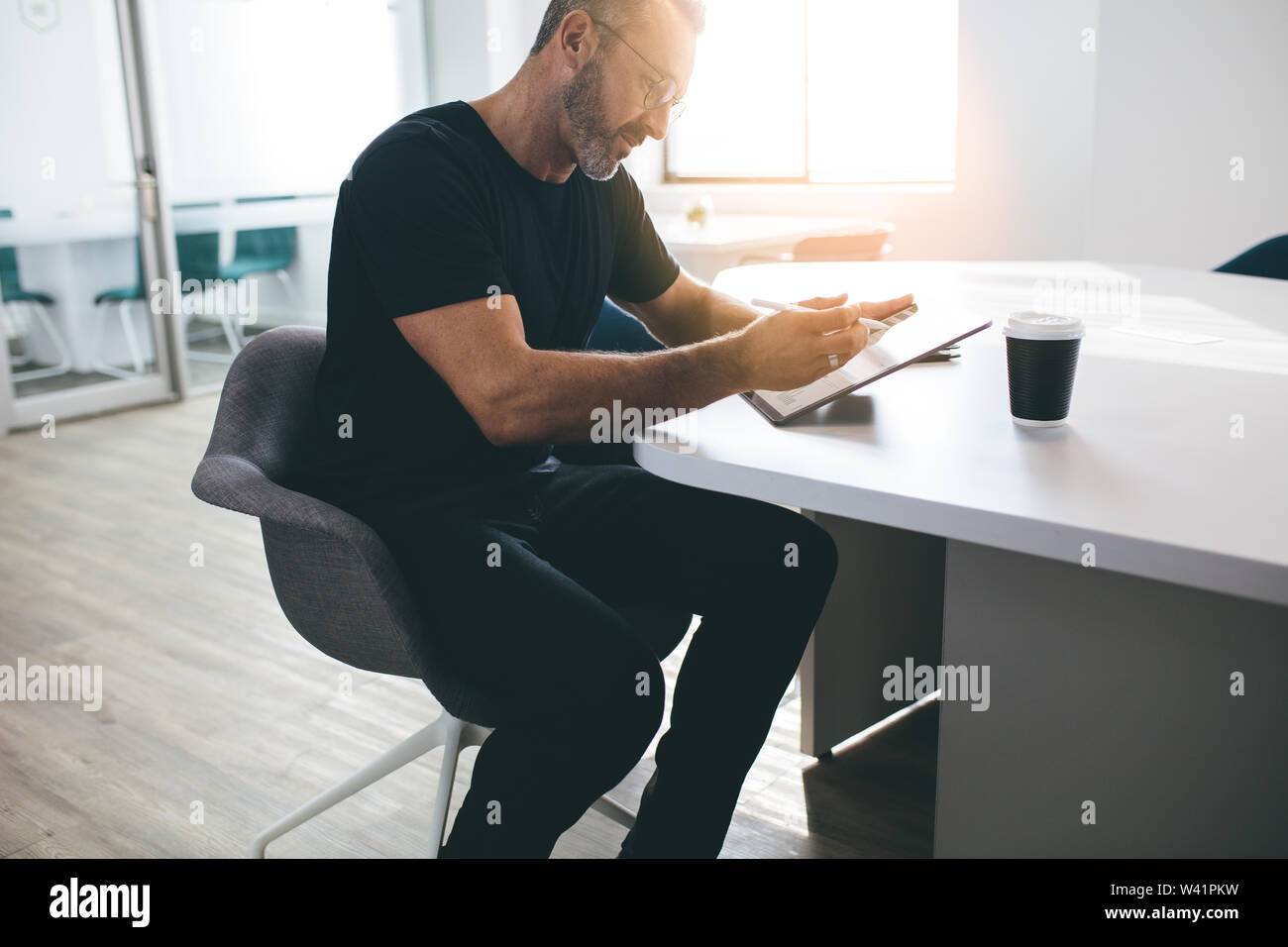 Imprenditore maschio con tavoletta digitale in ufficio. Imprenditore utilizzando tablet pc durante la seduta a tavola in luminoso spazio in ufficio. Foto Stock