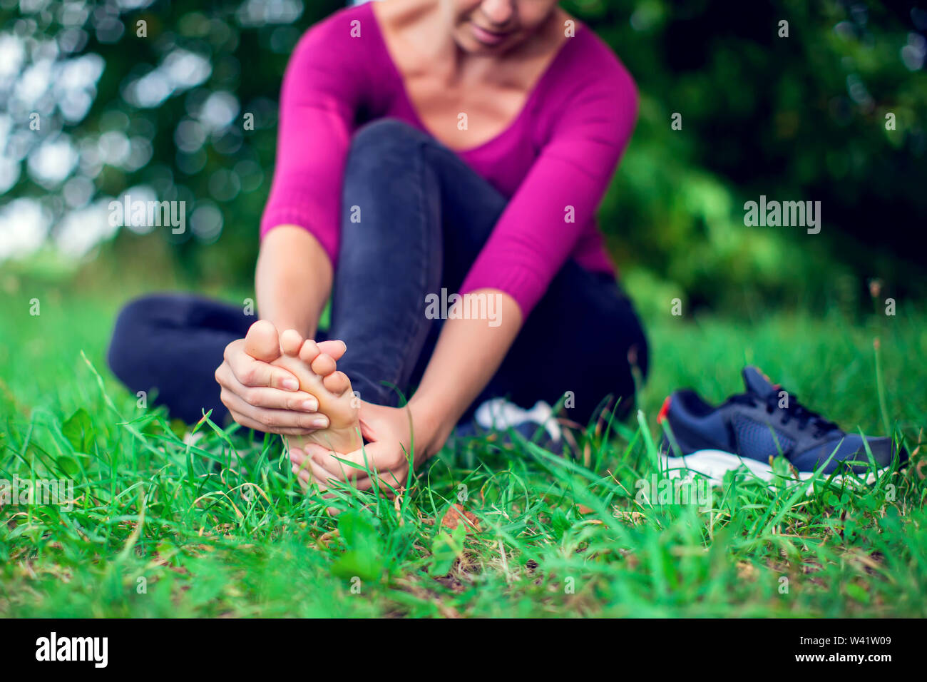 Il dolore del piede .donna seduta sull'erba. La sua mano catturati al piede.  Avente piedi dolorosi e stiramento dei muscoli fatica per alleviare il  dolore. Concetto di salute Foto stock - Alamy