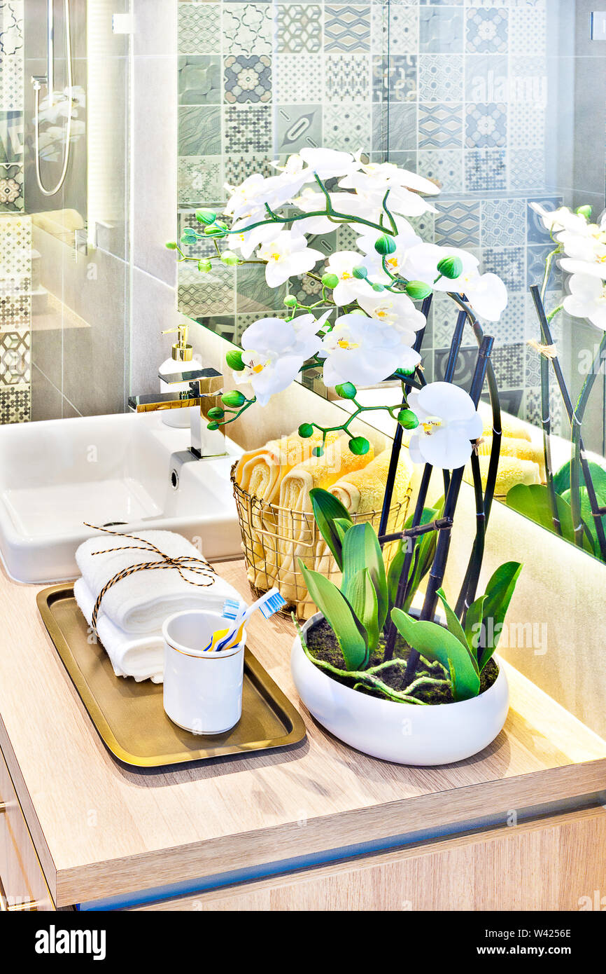 Bagno moderno fiore bianco decorazione sul bancone ligneo alto, lo specchio  sulla parete con la riflessione vicino gli asciugamani sulla griglia in  metallo crogiolatevi Foto stock - Alamy