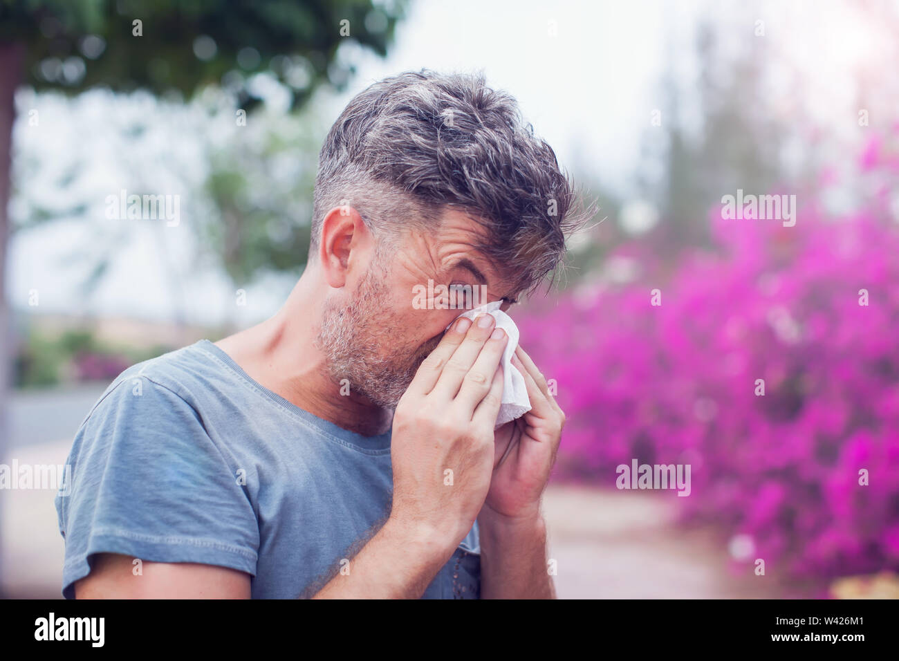 Uomo di starnuti ripetuti in un tessuto all'esterno. Allergia ai pollini primavera. Foto Stock