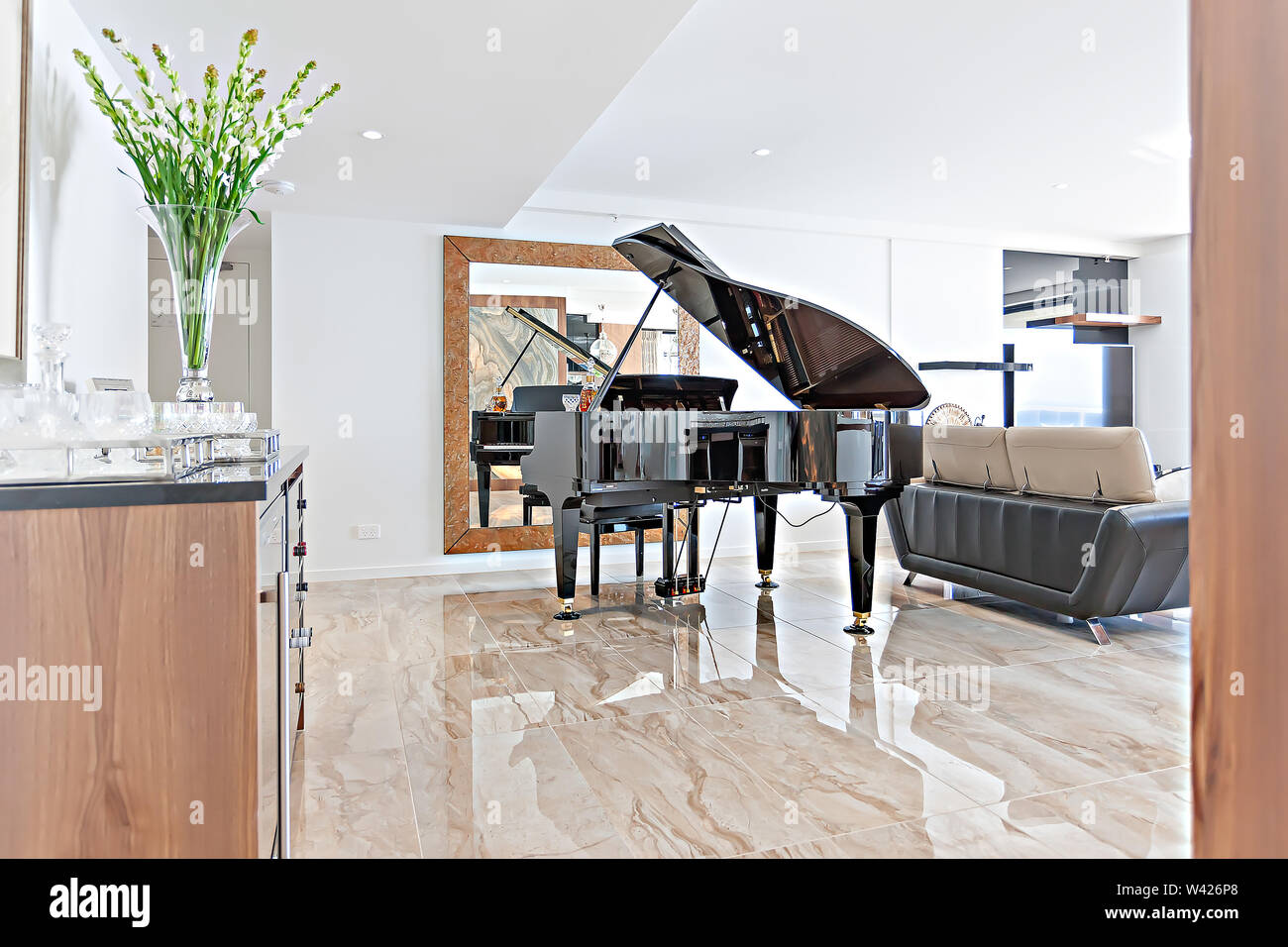 Area di soggiorno spaziosa con pavimento piastrellato, una casa bar, un gran pianoforte e uno specchio sul retro Foto Stock